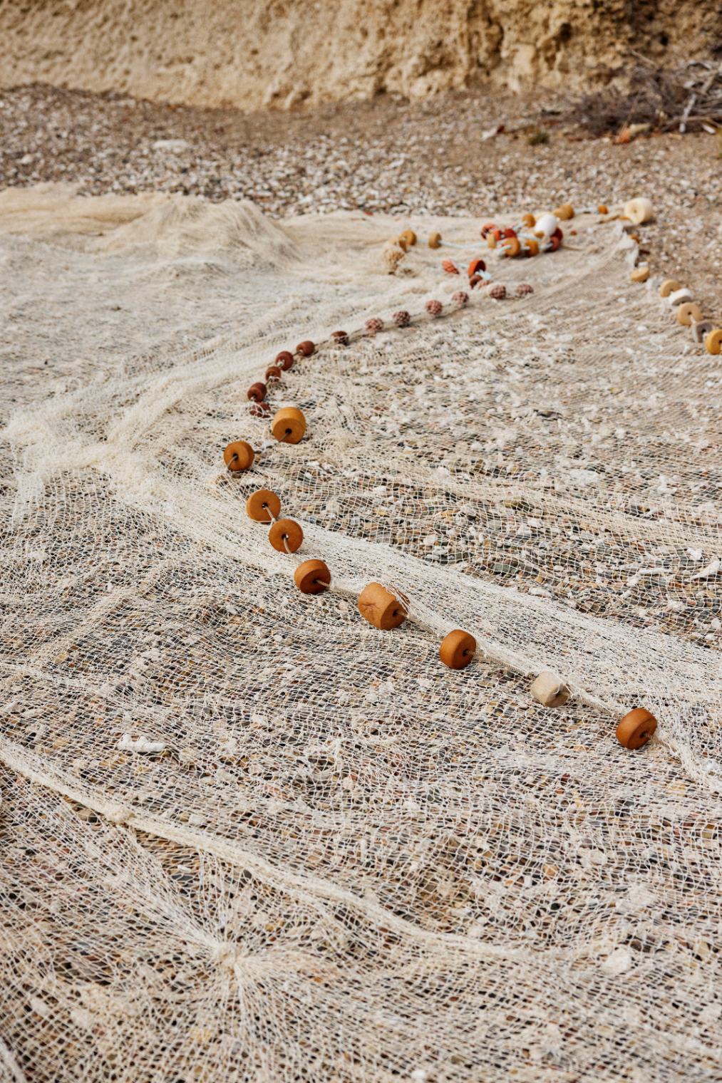 White fishing nets with wooden floats resting on a pebbly beach.