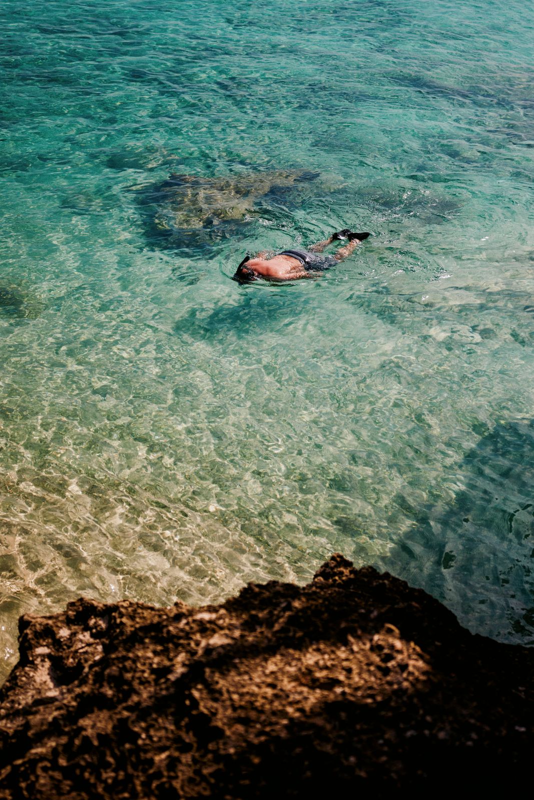 Swimmer snorkeling in clear turquoise Caribbean water over rocky ocean floor.