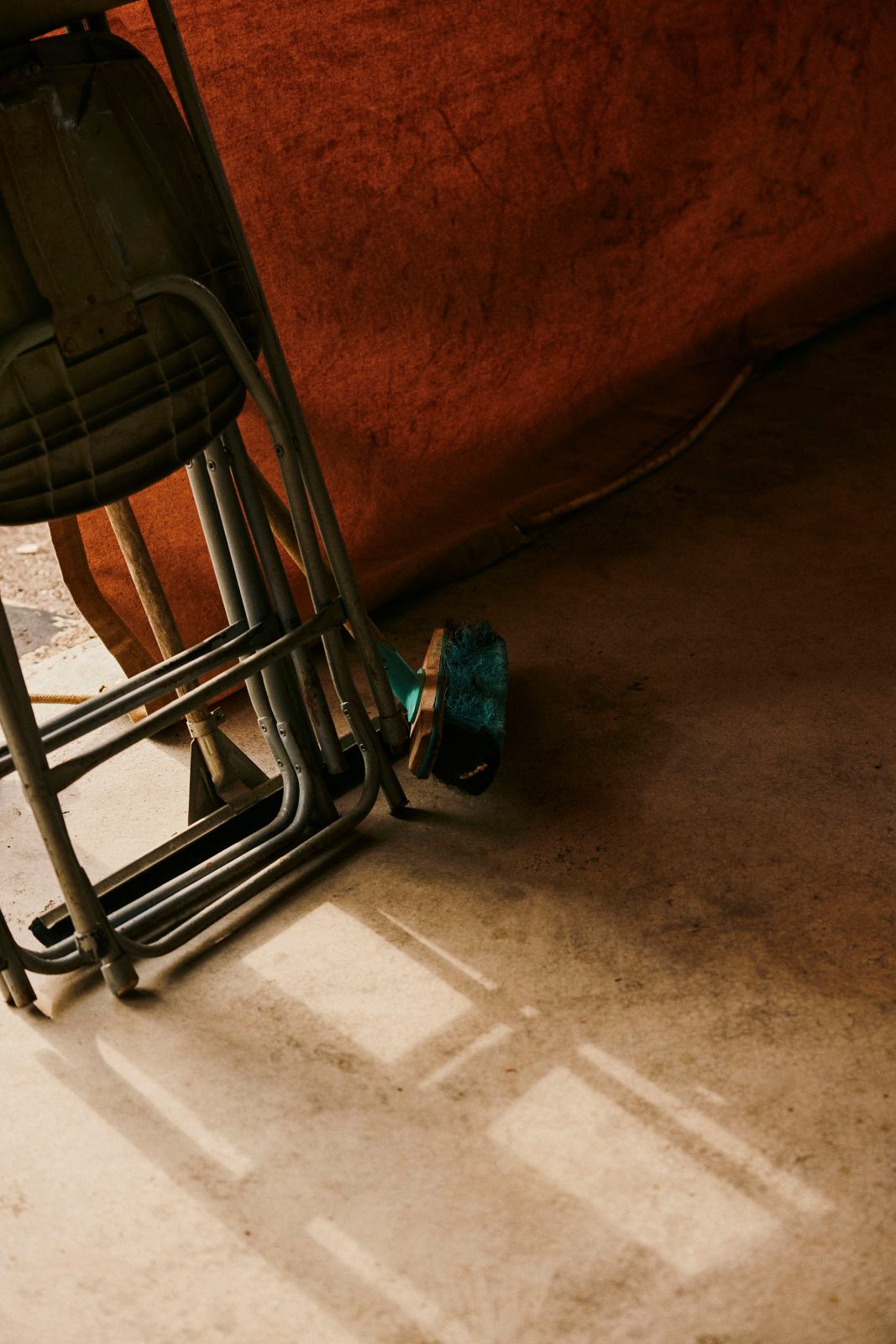 Push broom and folded chairs inside a dusty garage illuminated by sunlight.