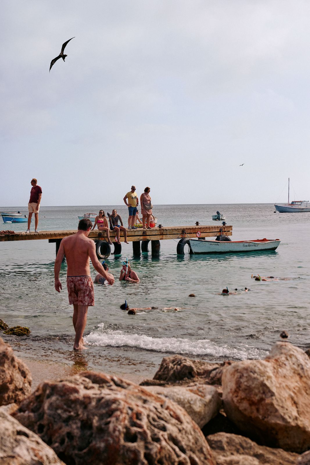 People snorkeling in clear water near a wooden pier under bright sky.