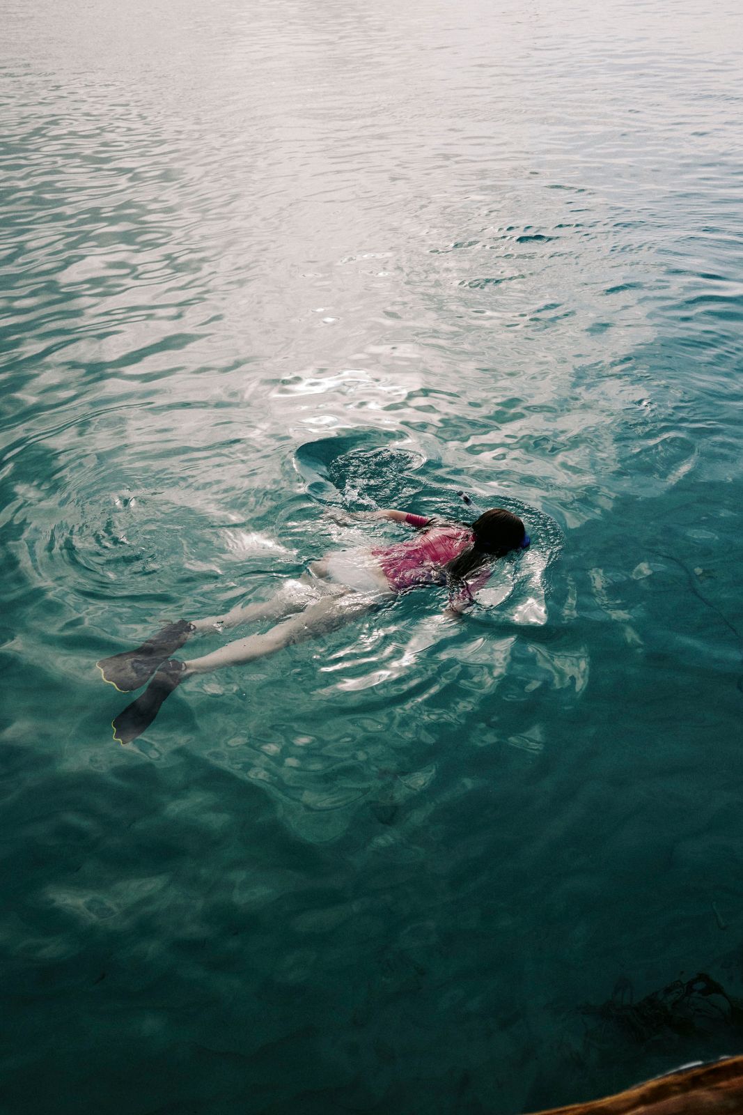 Swimmer in pink swimwear snorkeling through shimmering turquoise waters in daylight.