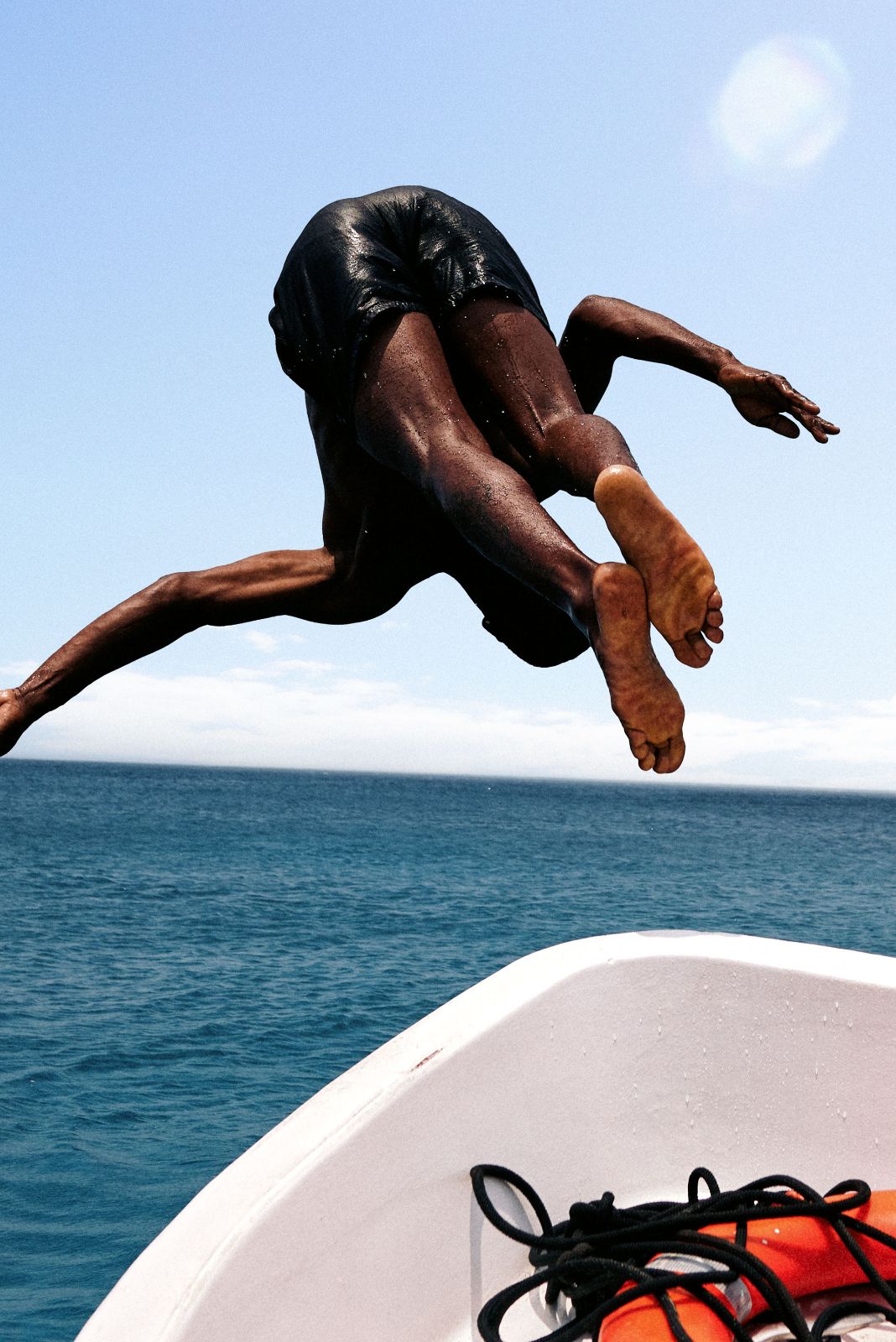 Person diving from boat into the deep blue ocean under bright sunlight.