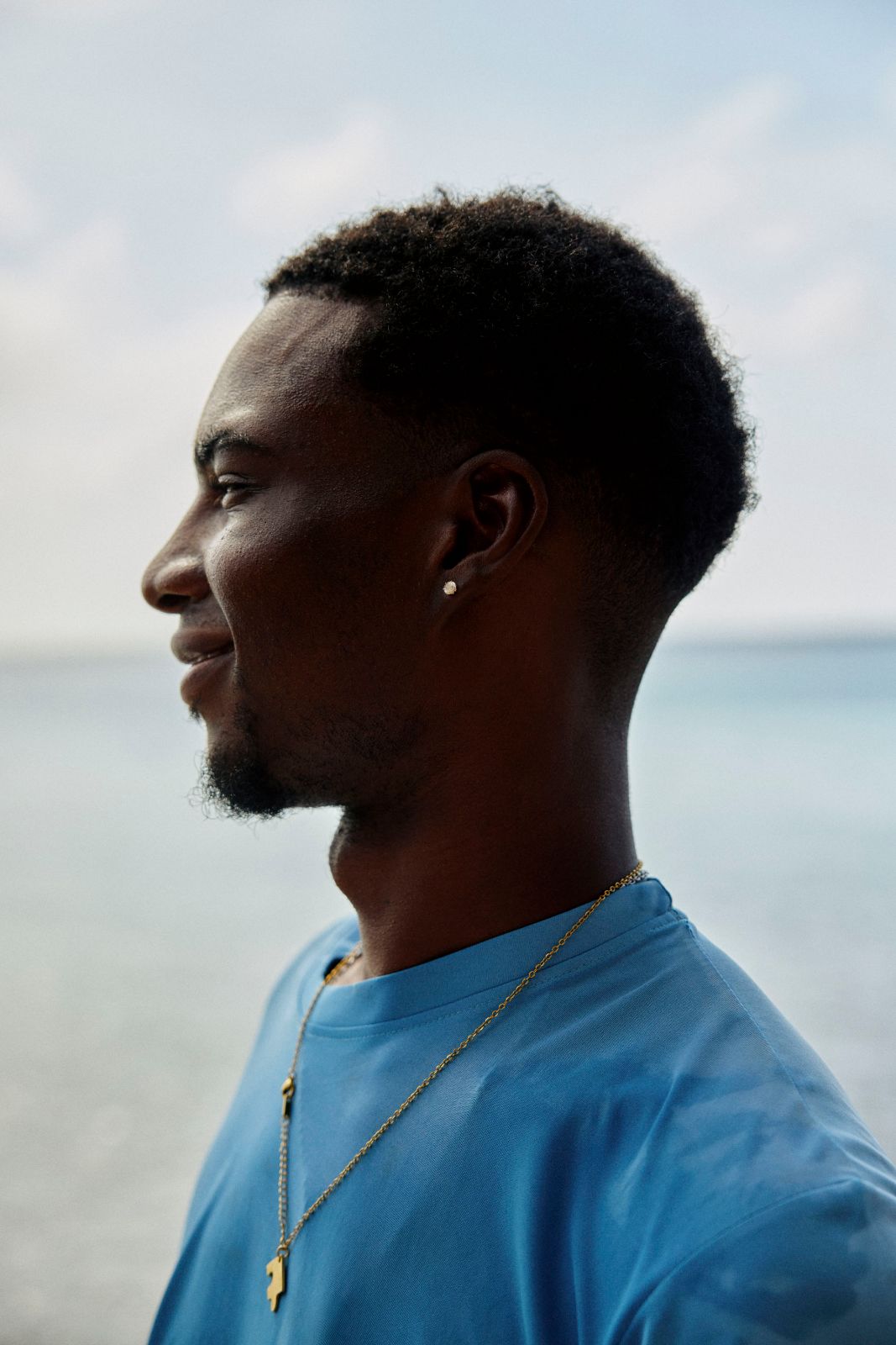 Profile of a young man smiling against a bright hazy ocean horizon.