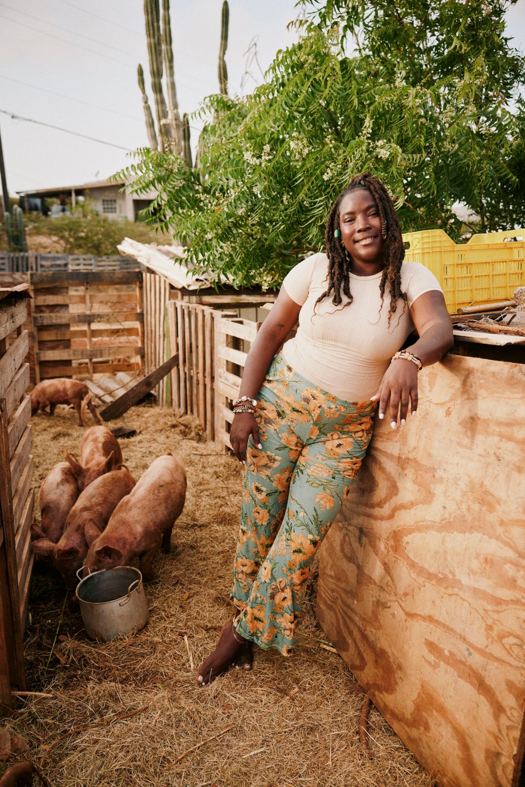 Smiling woman leaning against wooden pig enclosure on a rural farm.