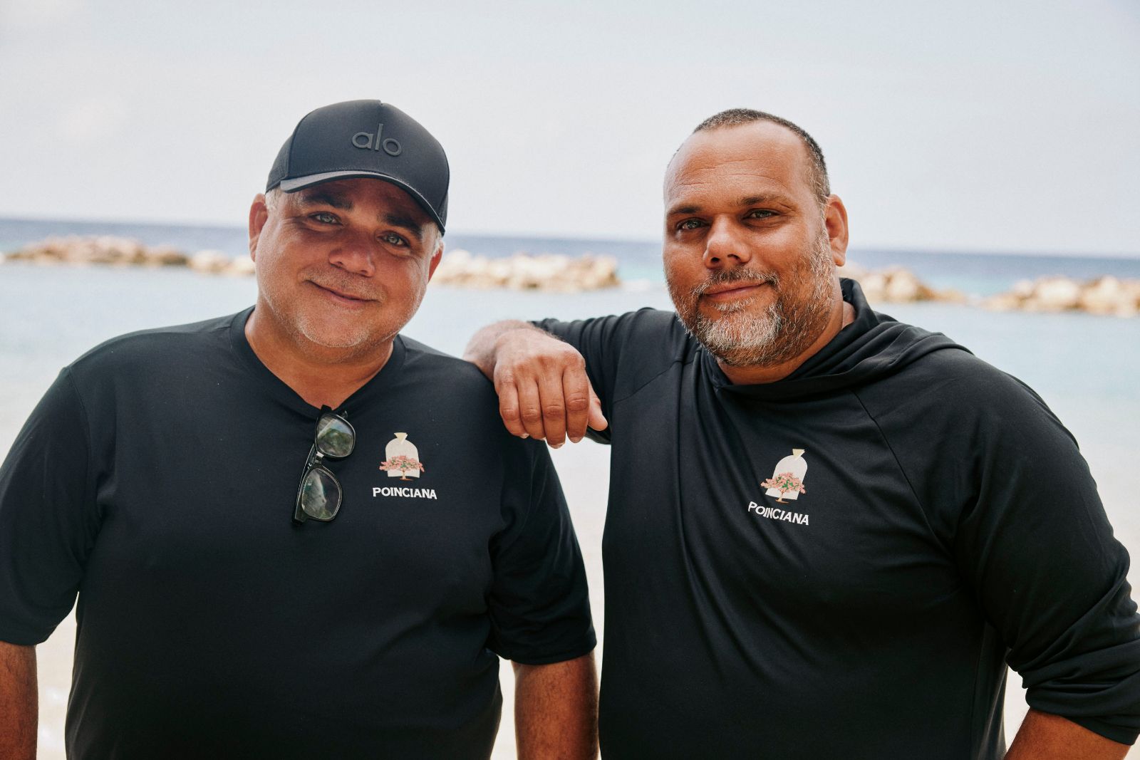 Two men in black shirts standing happily together on a sunny beach.
