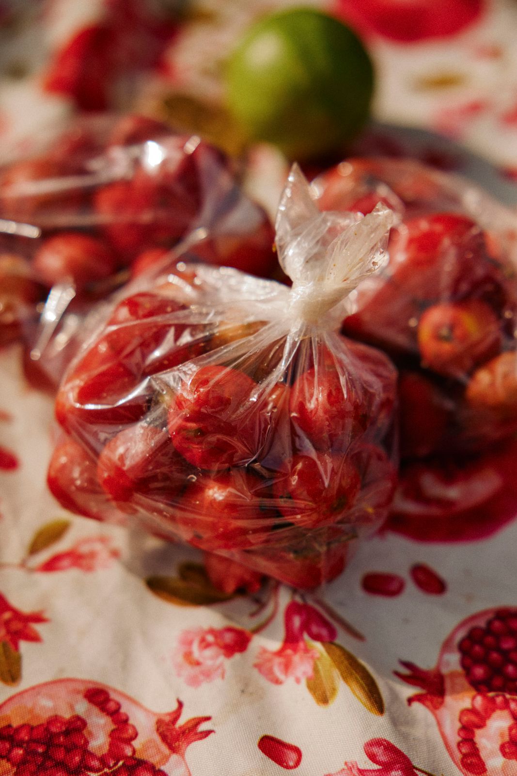 Small red fruits in knotted plastic bags on a floral patterned tablecloth.