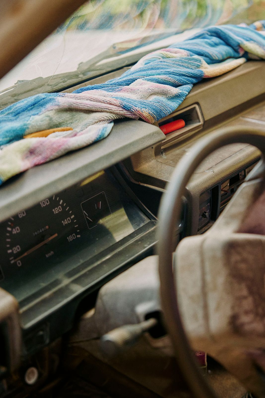 Striped towel on a vintage car dashboard with steering wheel and speedometer.