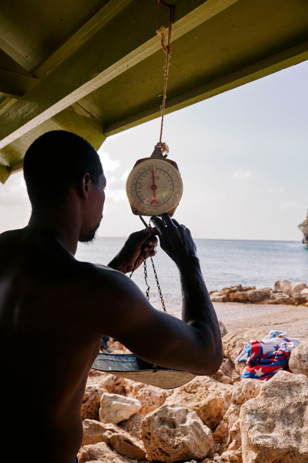 Silhouette of a fisherman adjusting a hanging metal scale by the ocean.