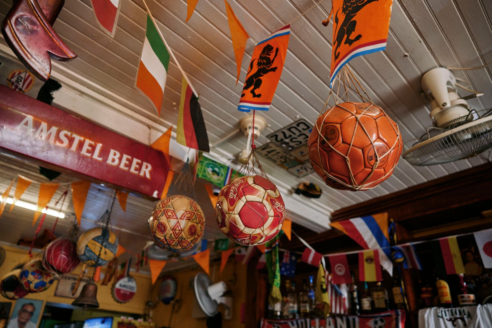 Hanging soccer balls and international flags inside a dimly lit local bar.