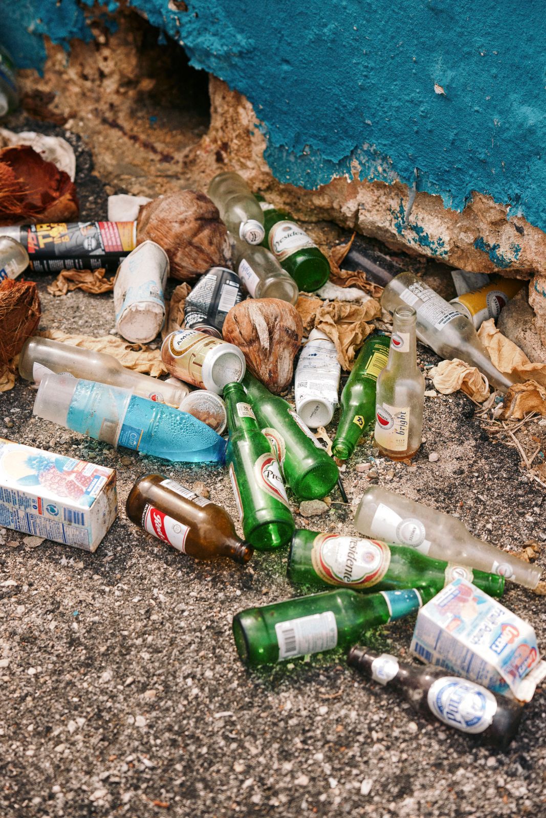 Litter of glass bottles and cans against a blue wall and stones.