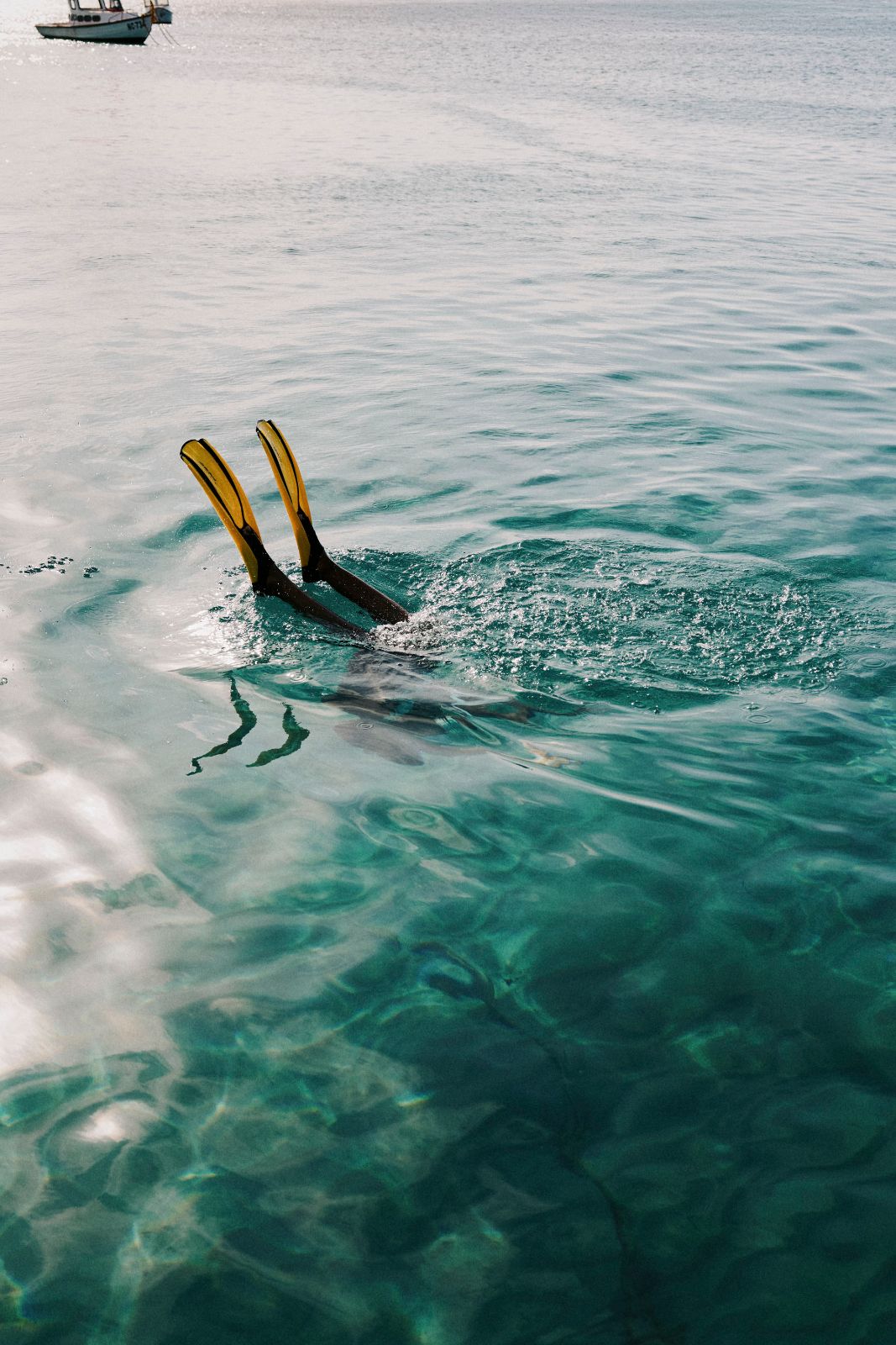Yellow diving fins breaking the surface of clear turquoise coastal waters.