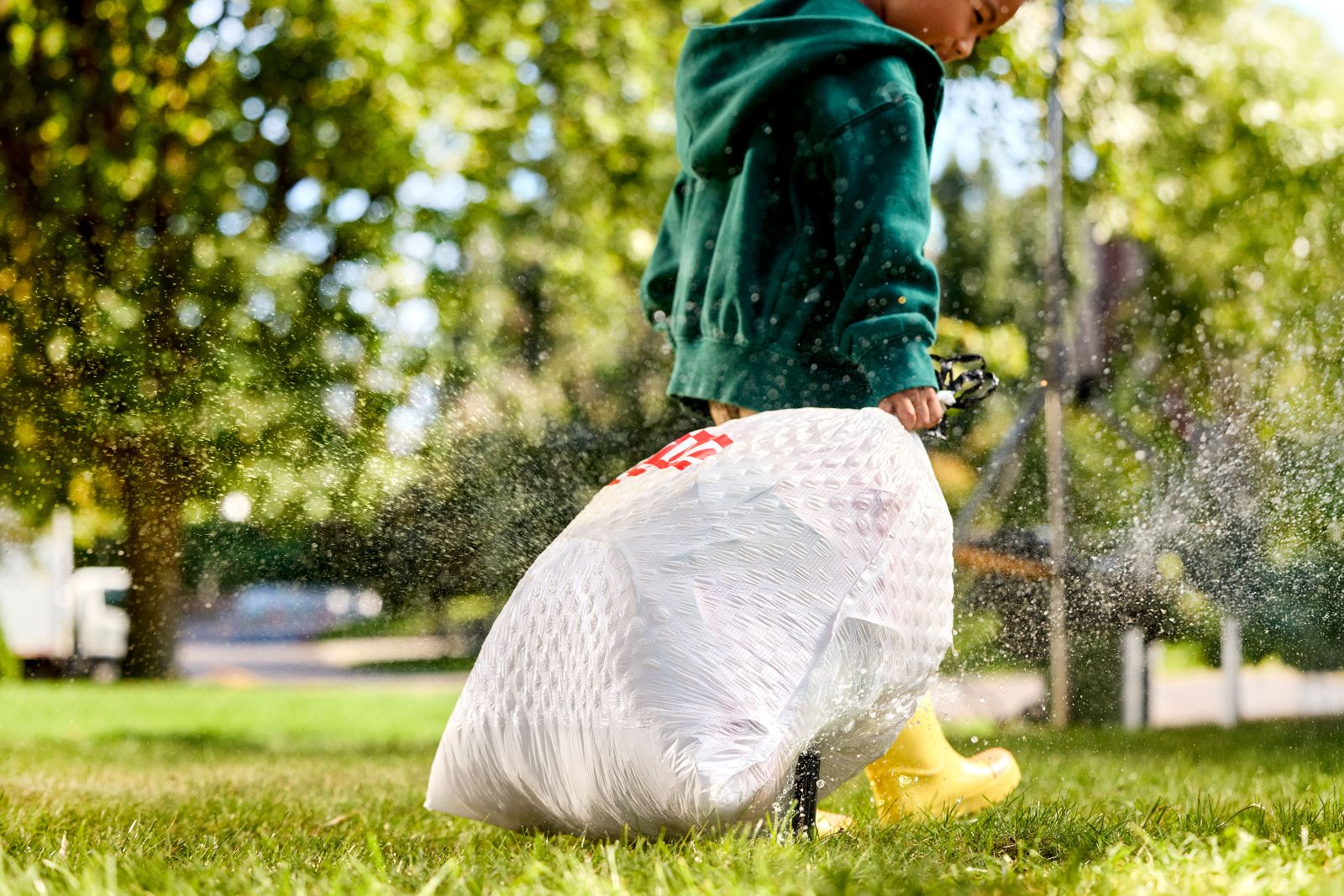 Low angle shot of a child pulling a heavy Glad bag across wet, sprinkler-soaked grass.