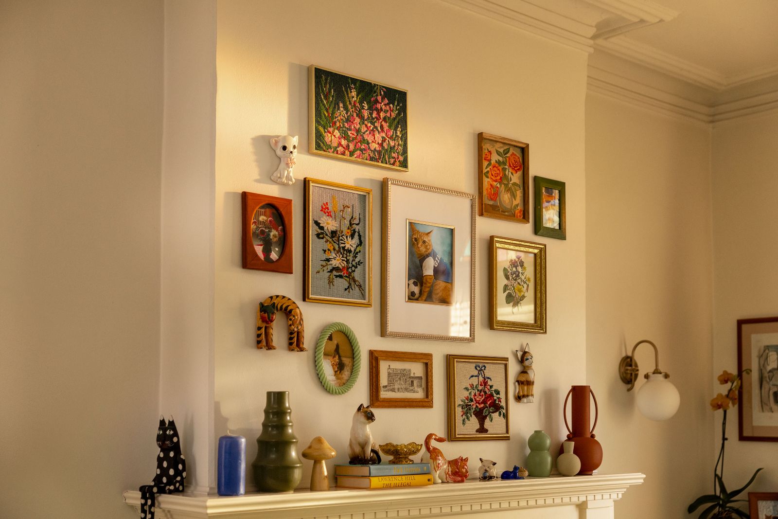 Wall decor featuring an eclectic mix of framed cat art and delicate ceramic figurines.