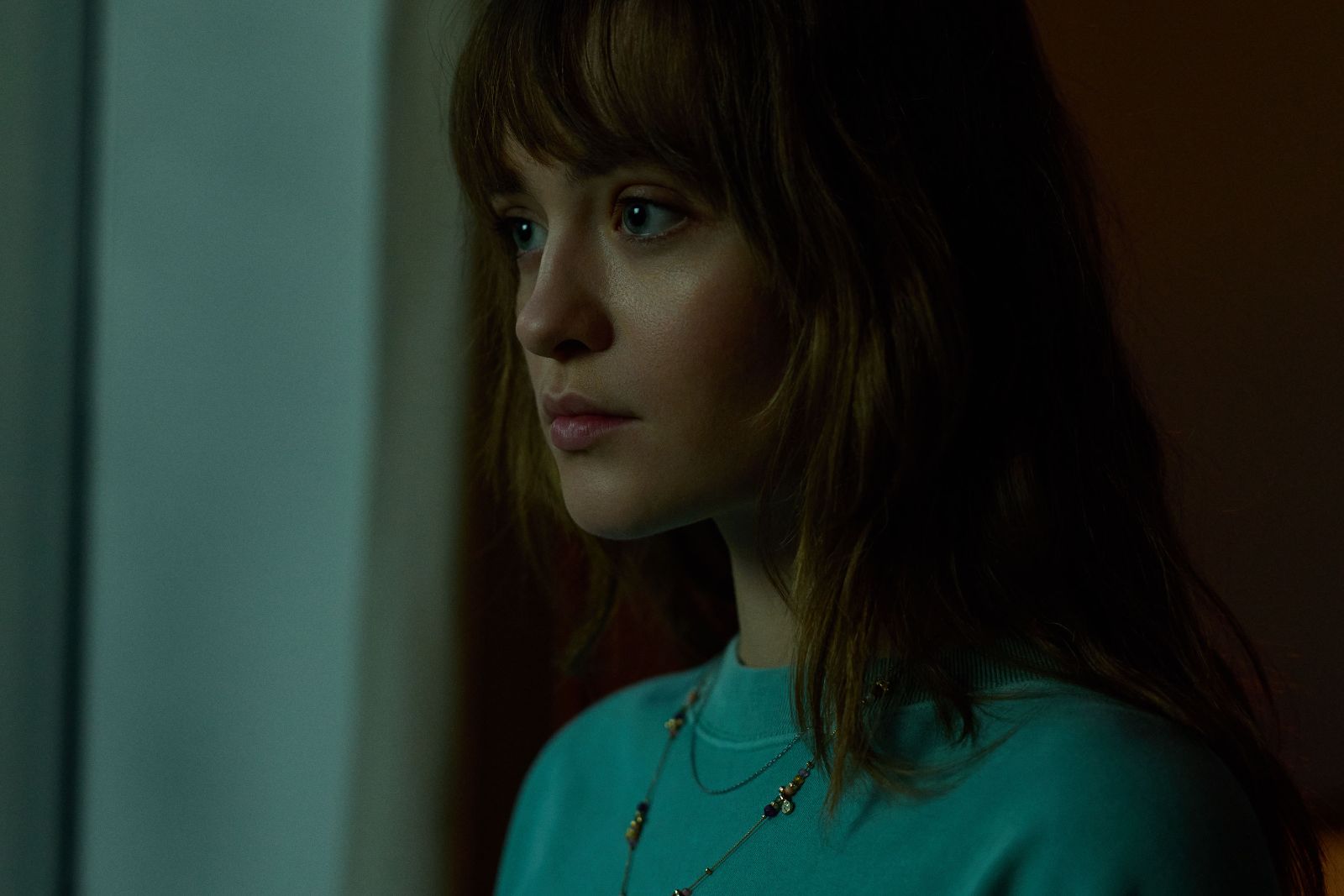 Close-up profile of a pensive young woman bathed in soft cyan window light.