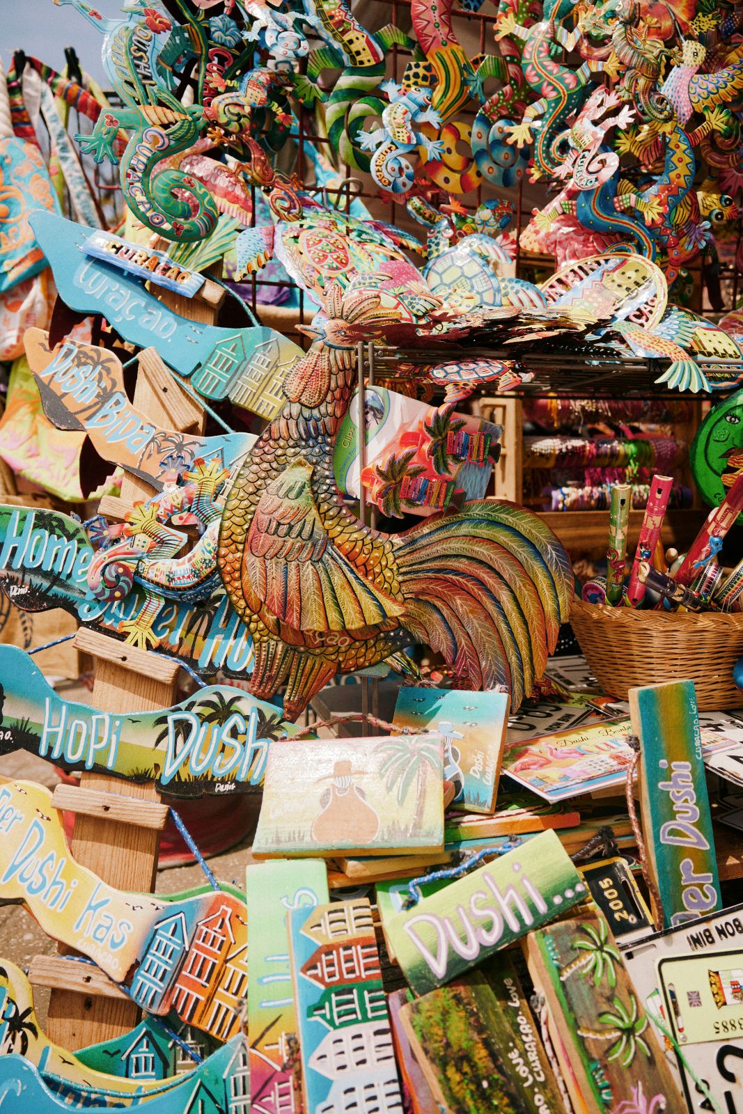 Colorful, hand-painted metal signs and animal souvenirs clustered tightly at a Curacao market.