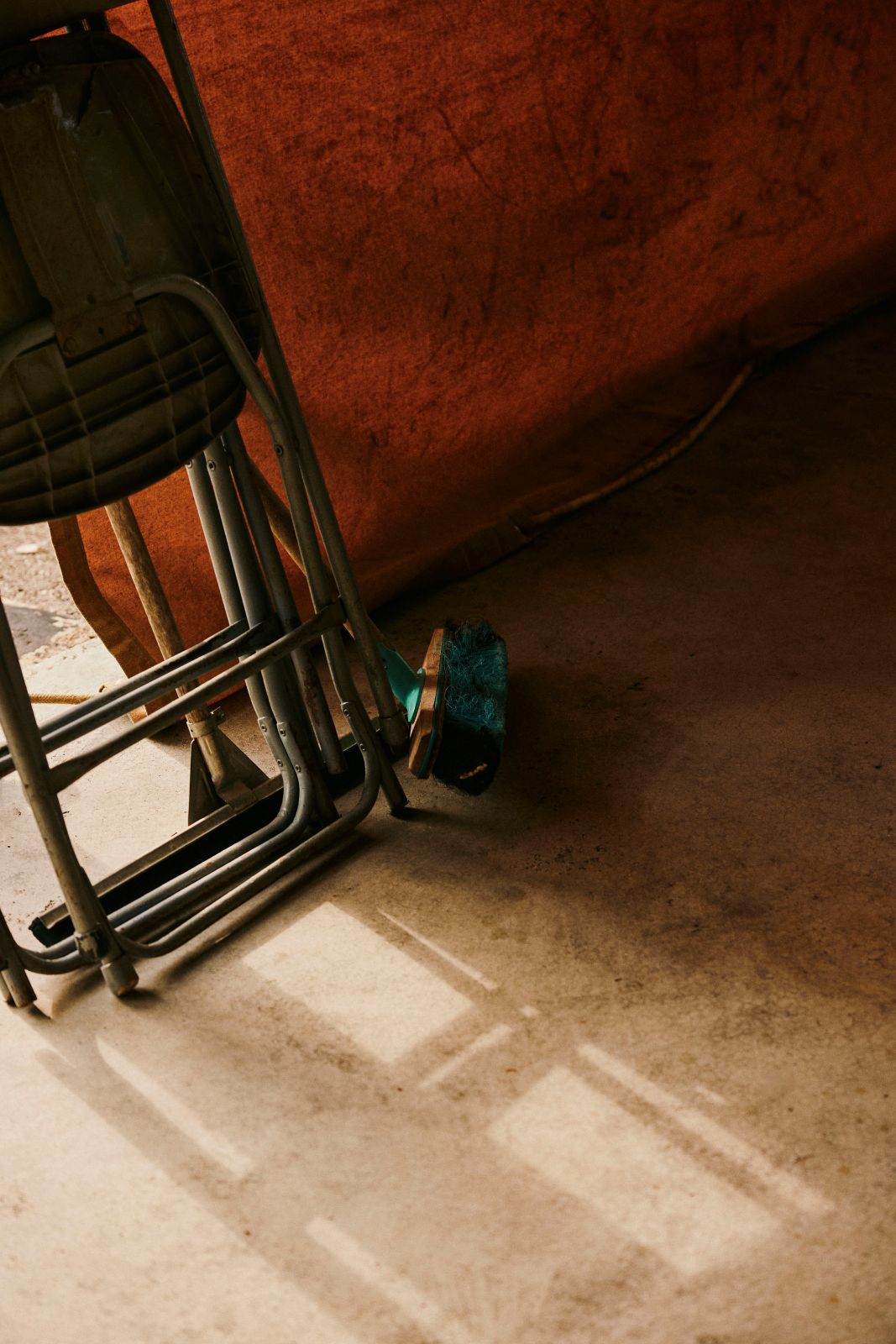 Folded metal chairs and a broom resting against an orange tarp in dim light.