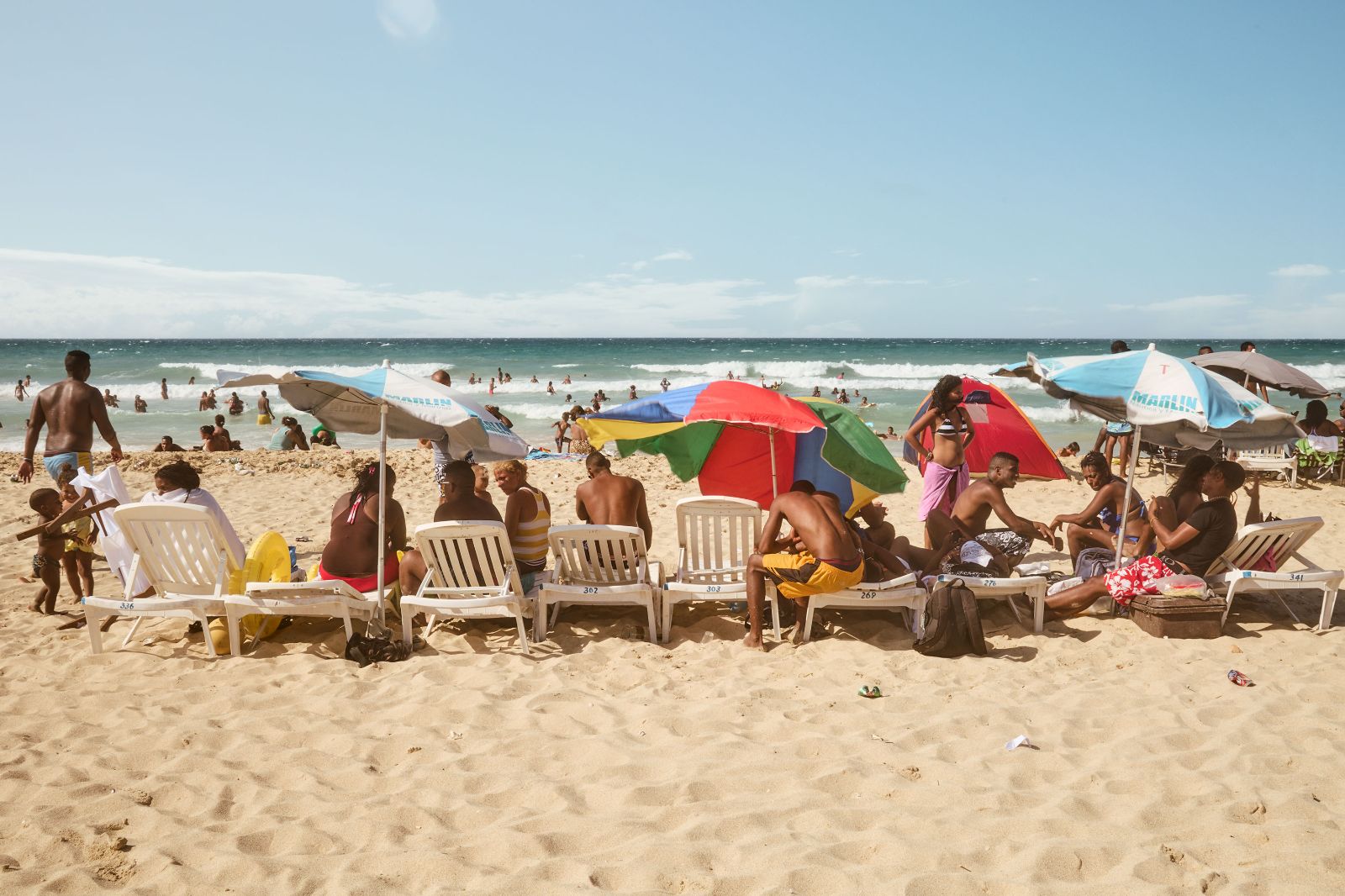 A wide view of a crowded beach lined with vibrant parasols and plastic chairs.