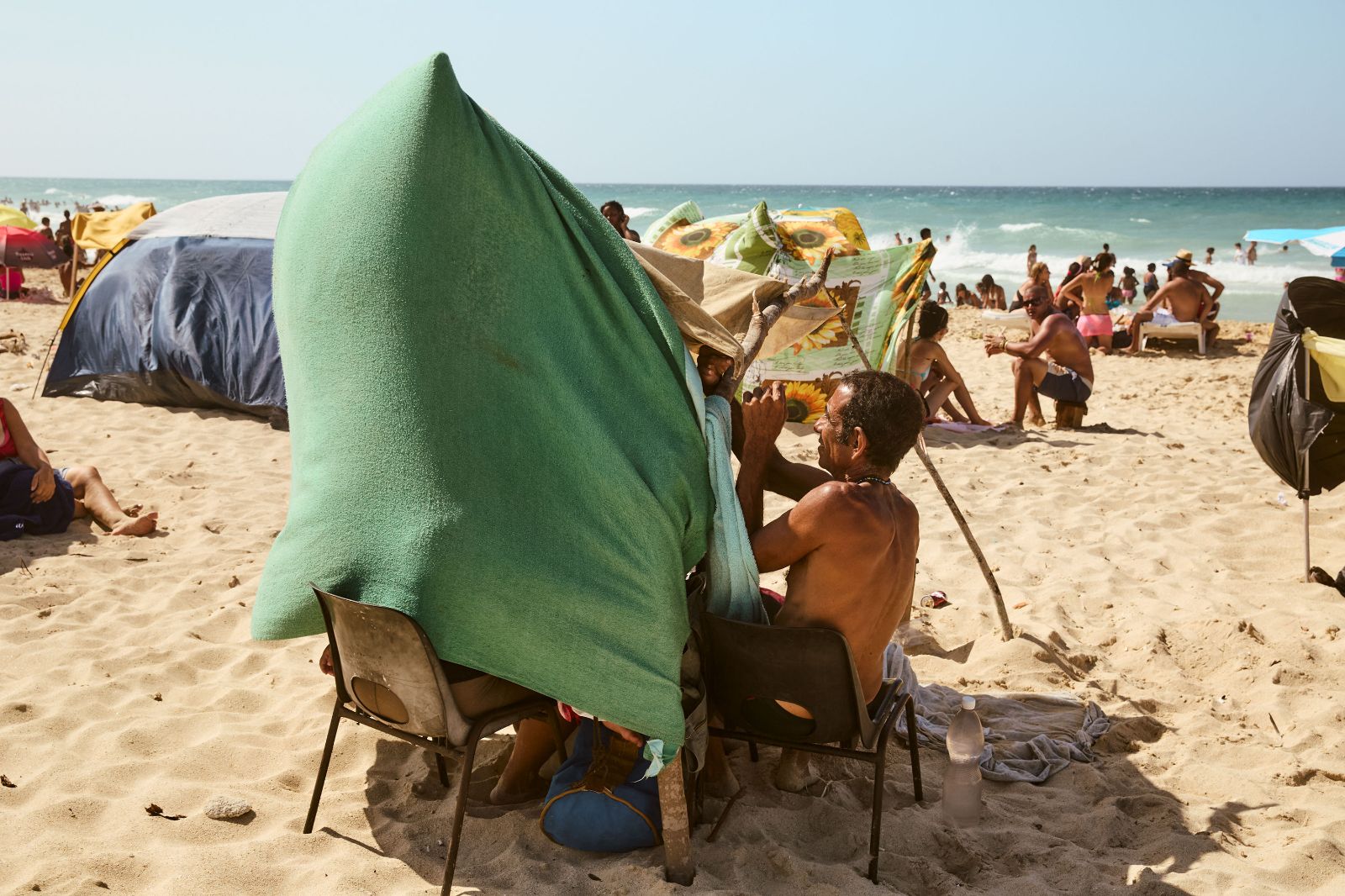 A Cuban man adjusts a resourceful, improvised sun tent made from a green towel.