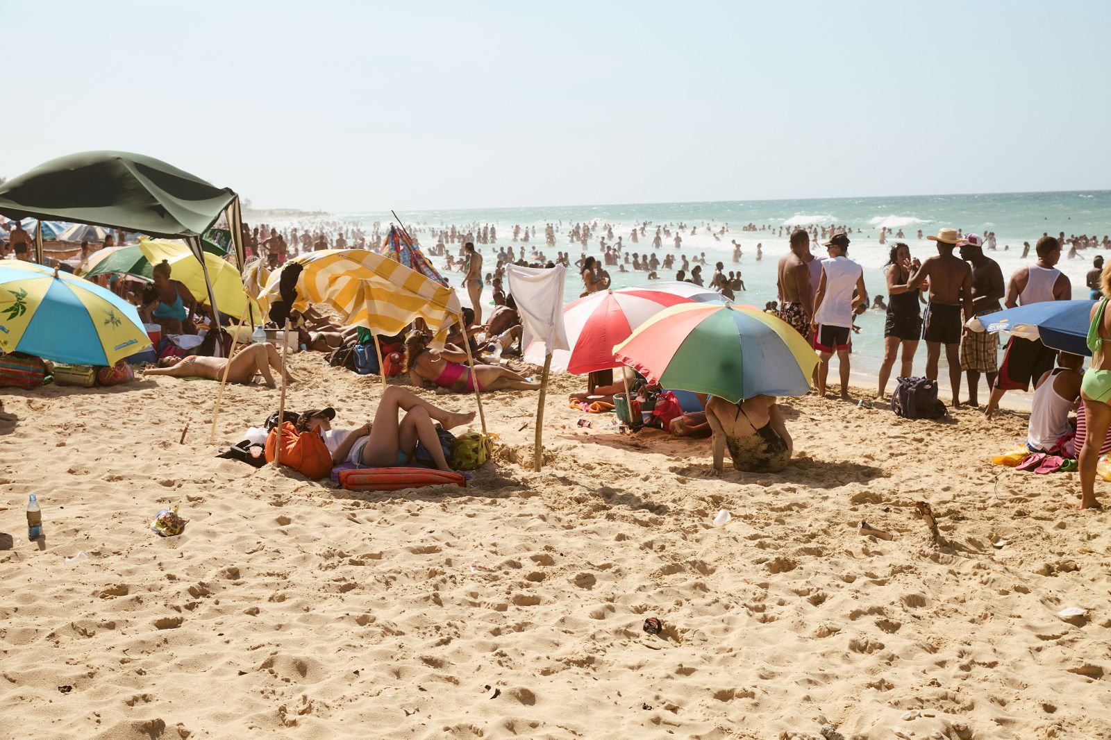Sunbathers relax beneath colorful striped umbrellas crowding a vibrant, sunlit Caribbean shoreline.
