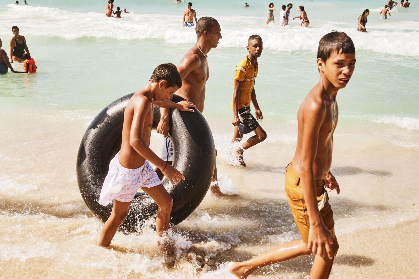 Young Cuban boys carry a massive inflated truck tire into the crashing ocean waves.
