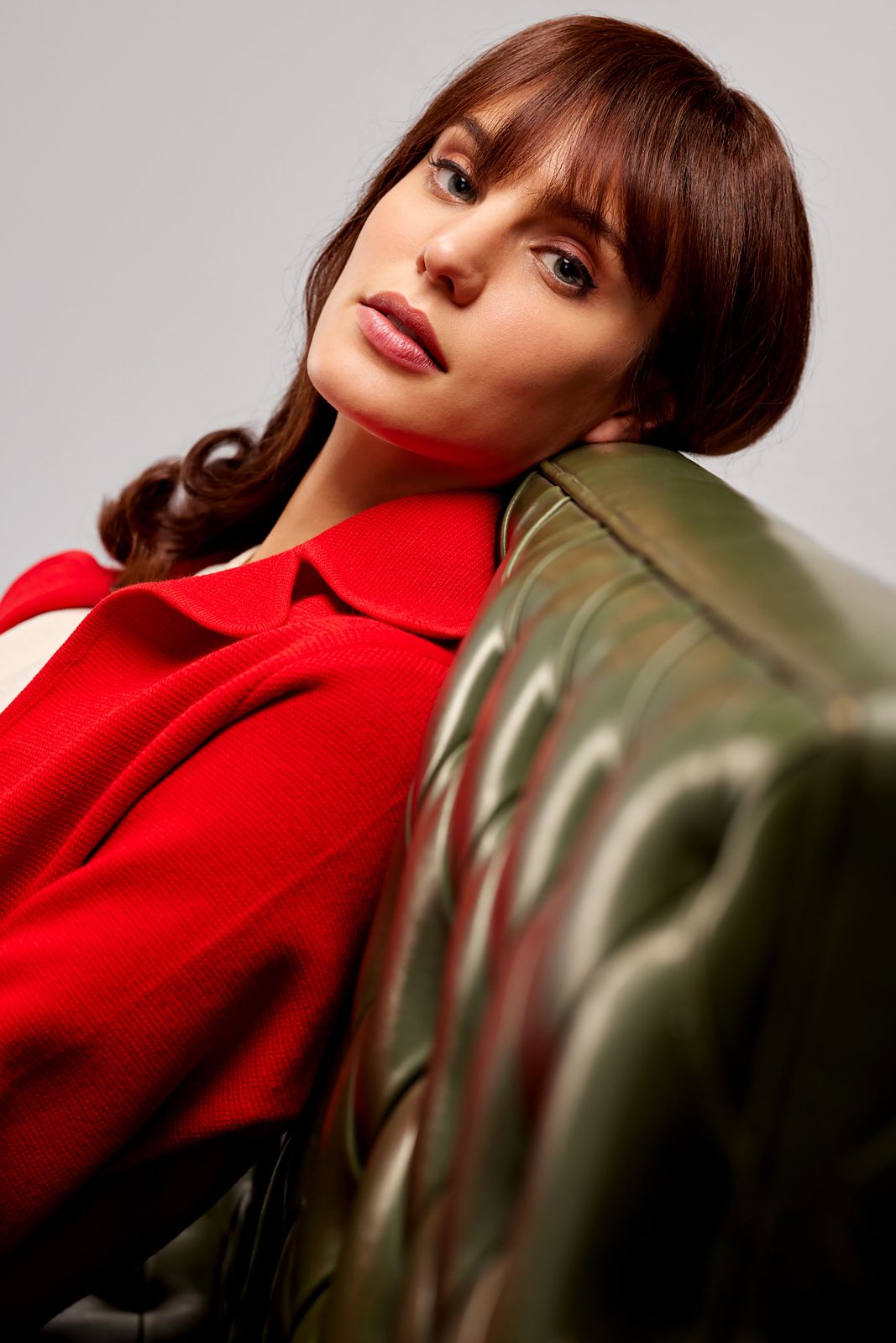 Macarena Achaga leaning back casually against a tufted green leather couch looking into the lens.