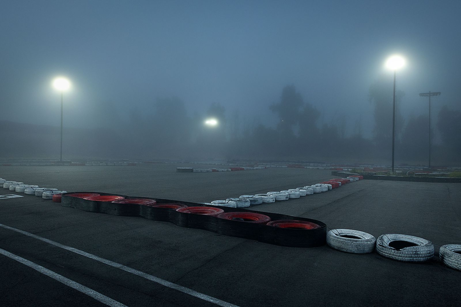 Low perspective of weathered racing tires bathed in moody halogen track illumination.