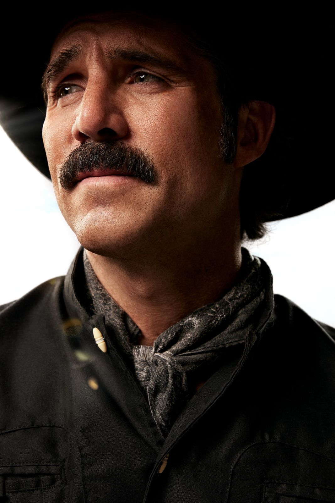 Close-up portrait of Jose Ron beneath a wide-brimmed hat, showcasing rugged details and textures.
