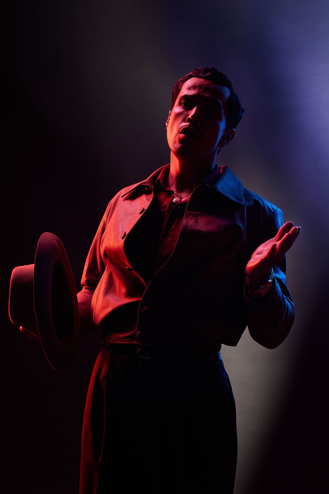 Actor Mario Moran caught mid-gesture, channeling Pedro Infante against a crimson and violet lit backdrop.