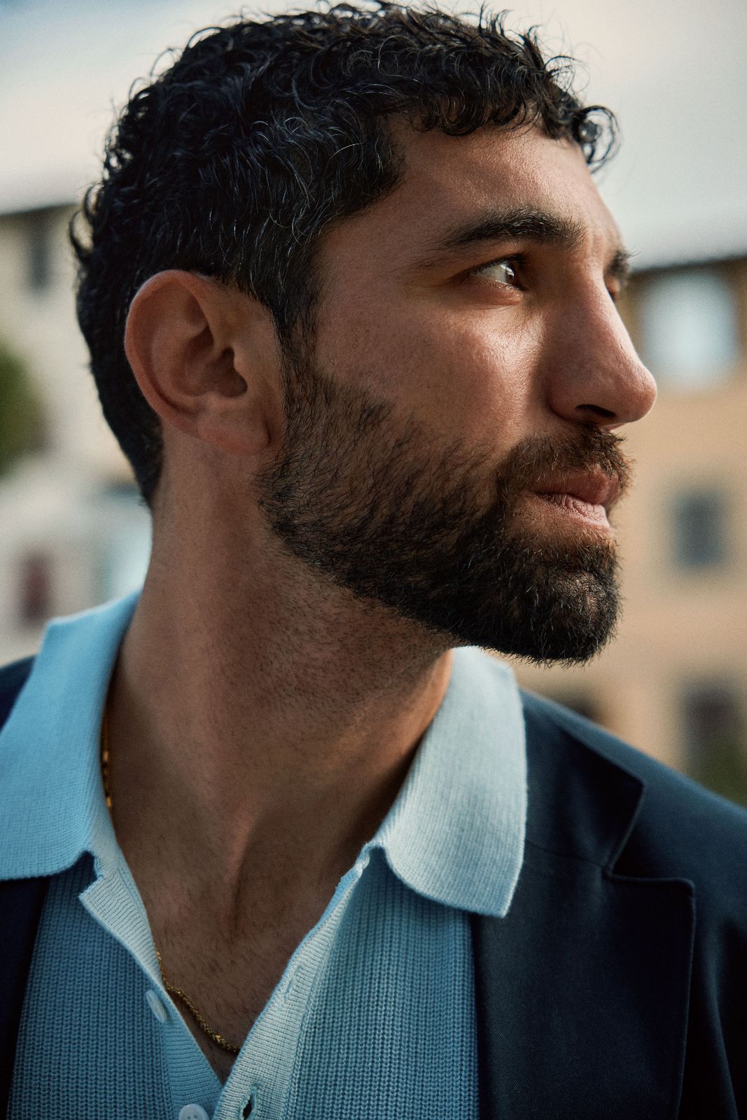 Close-up profile of a bearded man wearing a stylish navy blazer outdoors.