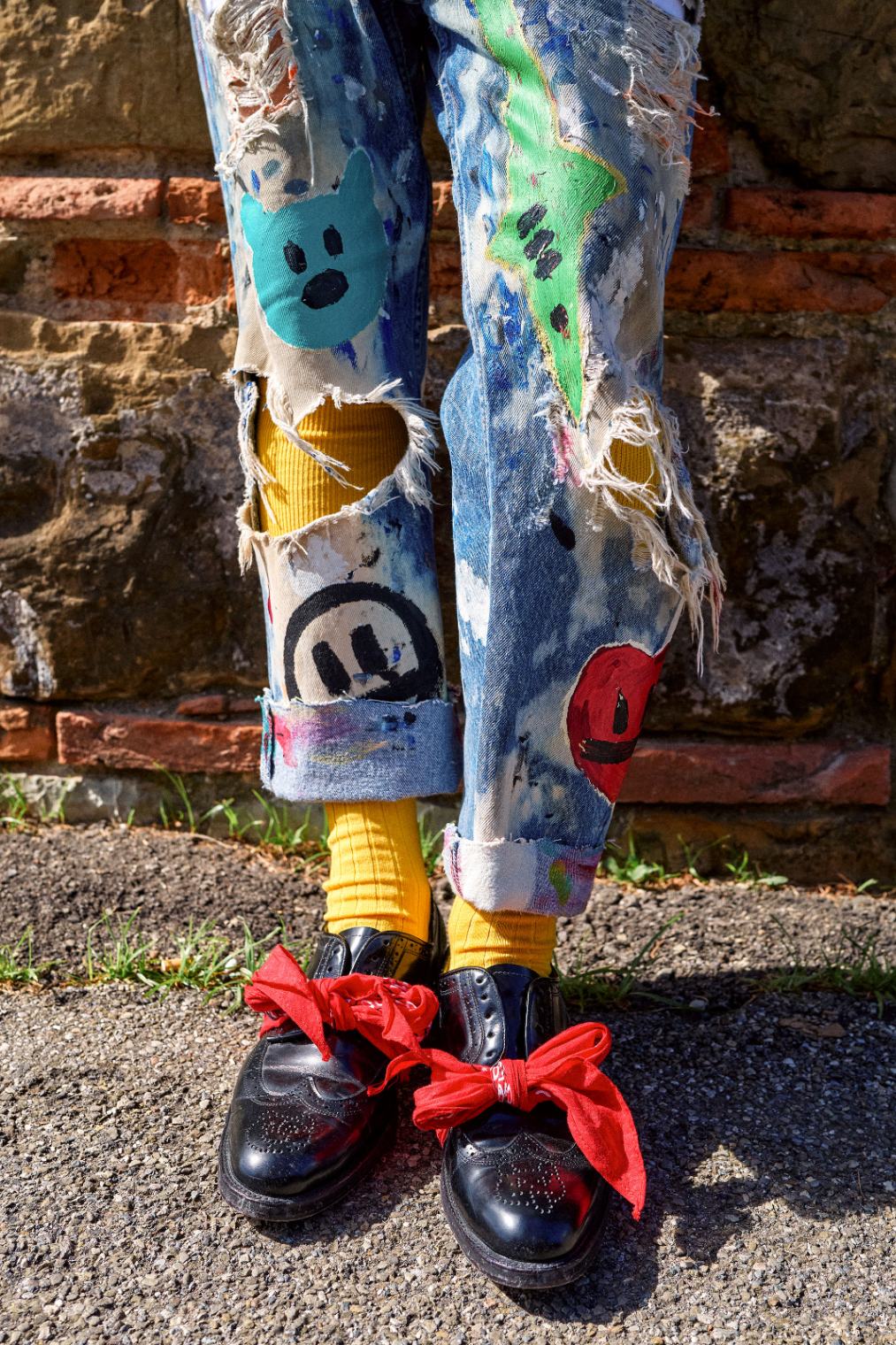 Detail of hand-painted distressed jeans above black oxfords with red bow laces.