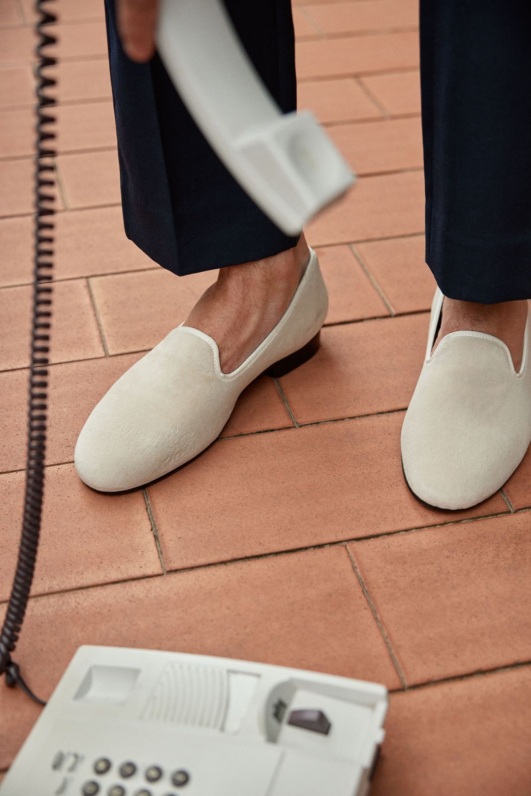 Close-up of white velvet loafers standing near a retro telephone receiver.