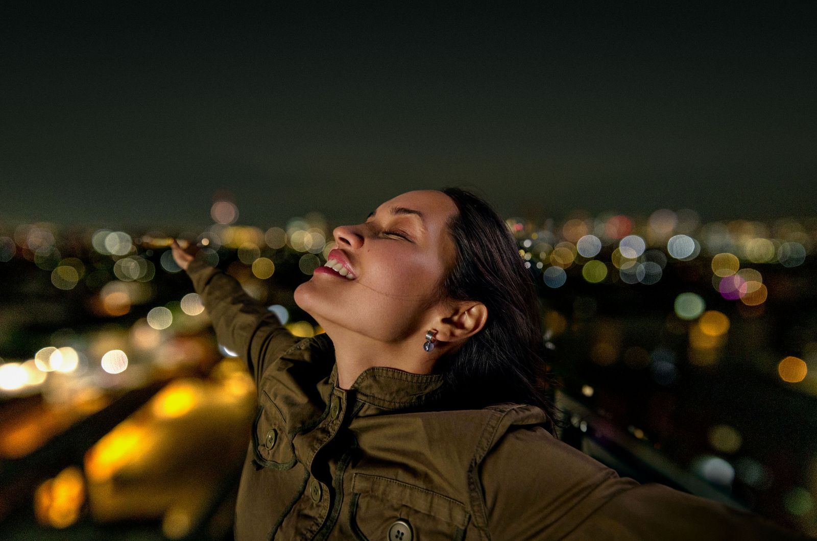 Woman smiling with eyes closed against a mesmerizing bokeh of Mexico City's glowing metropolis.
