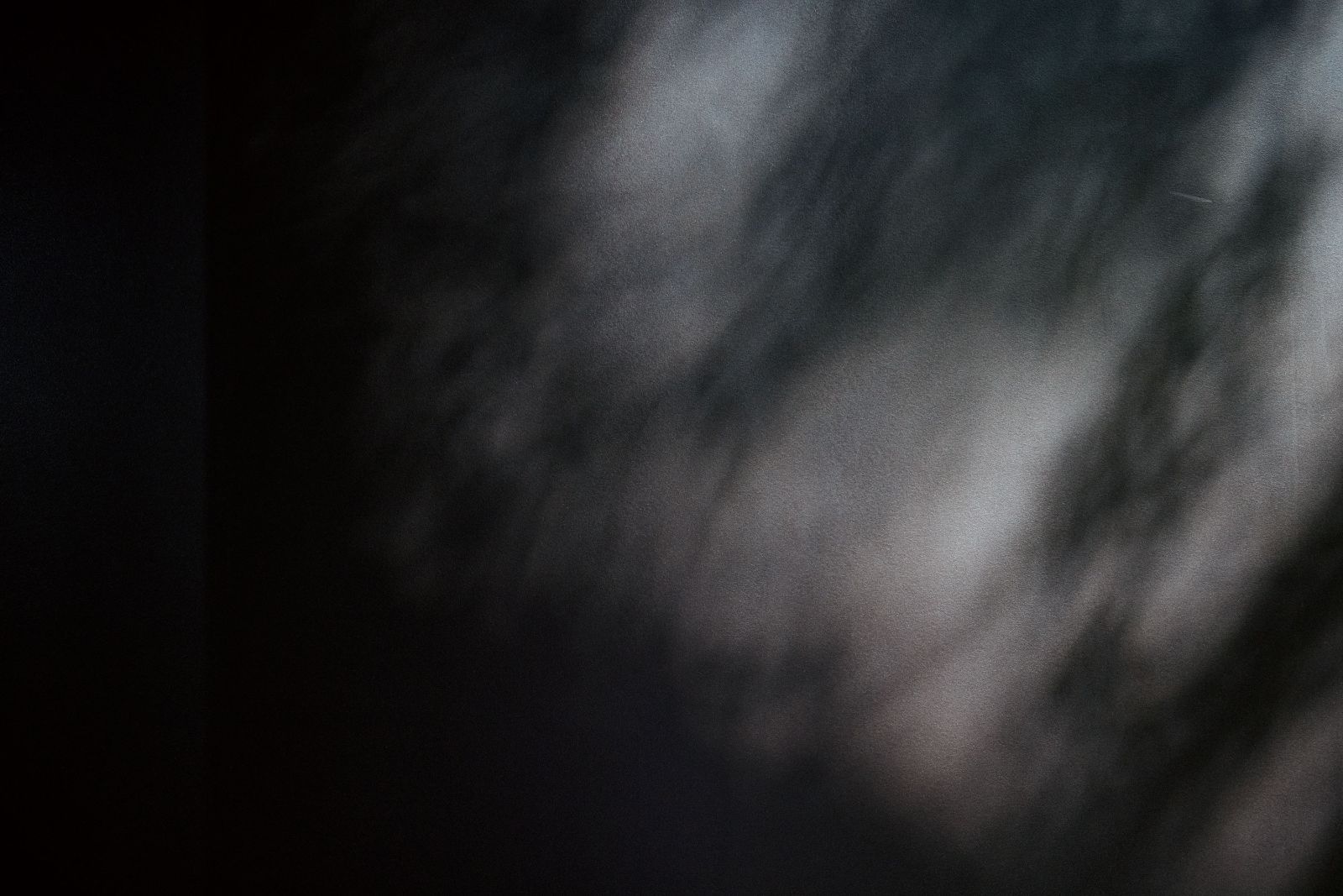 Abstract interplay of deep shadow and soft morning light on a textured dark wall.