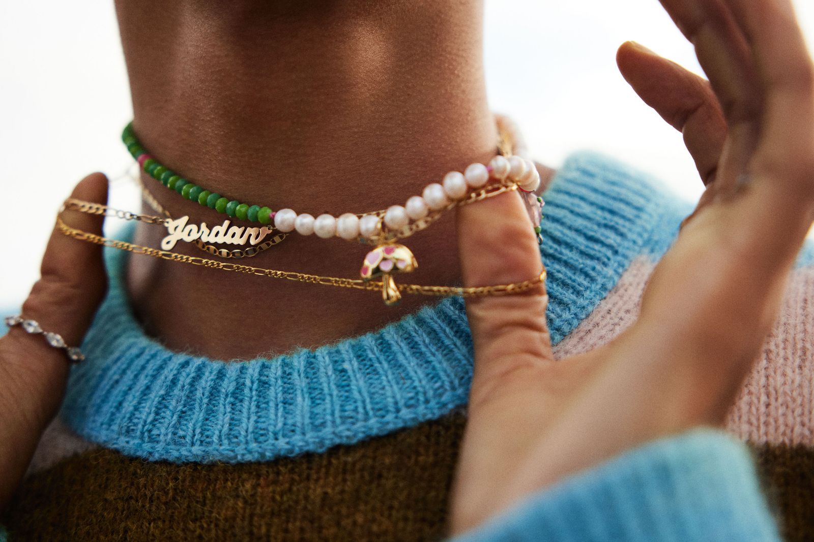 Close-up of layered pearl necklaces, green beads, and a gold mushroom pendant.