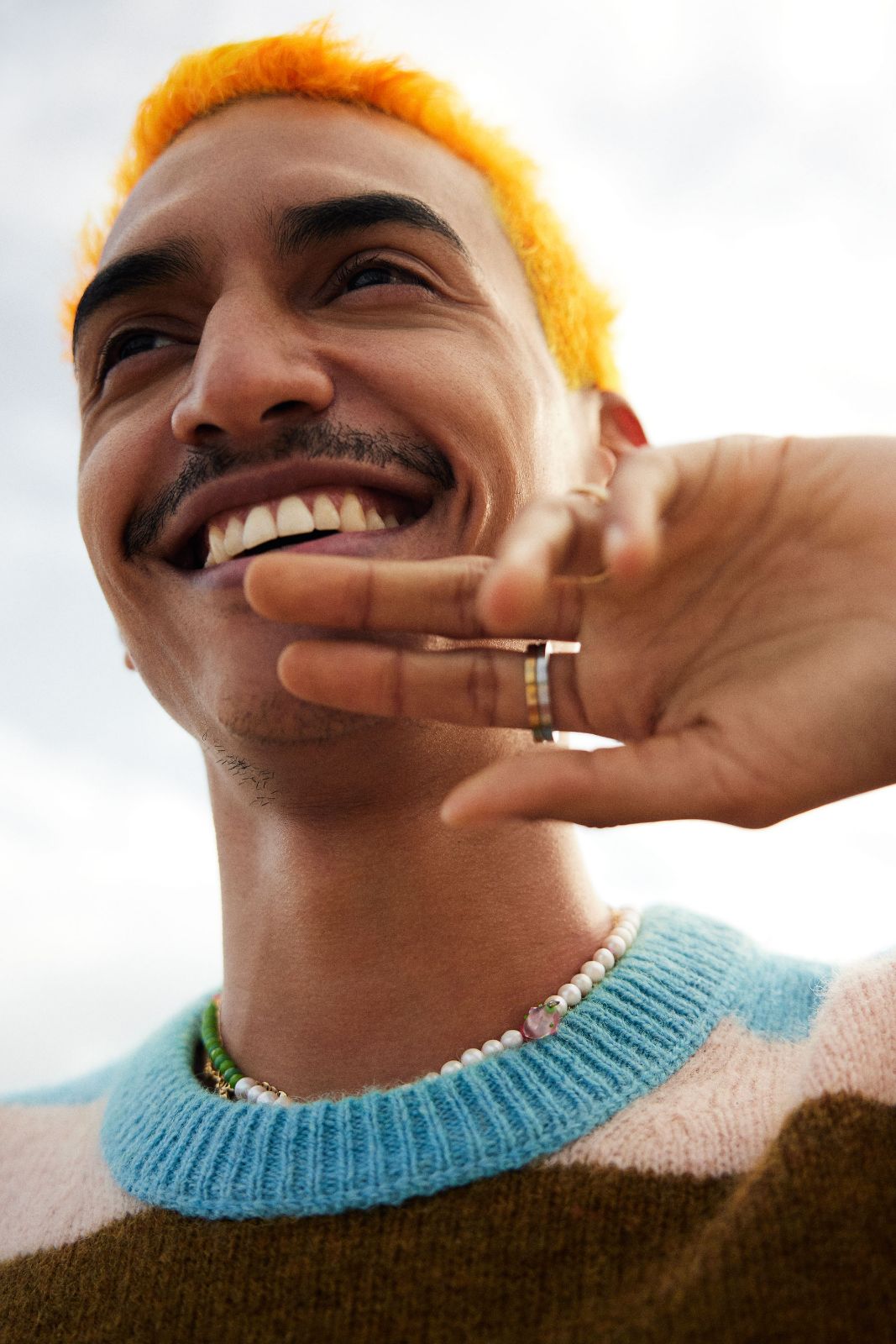 Close portrait of Flako smiling brilliantly while holding his ring-adorned hand up.