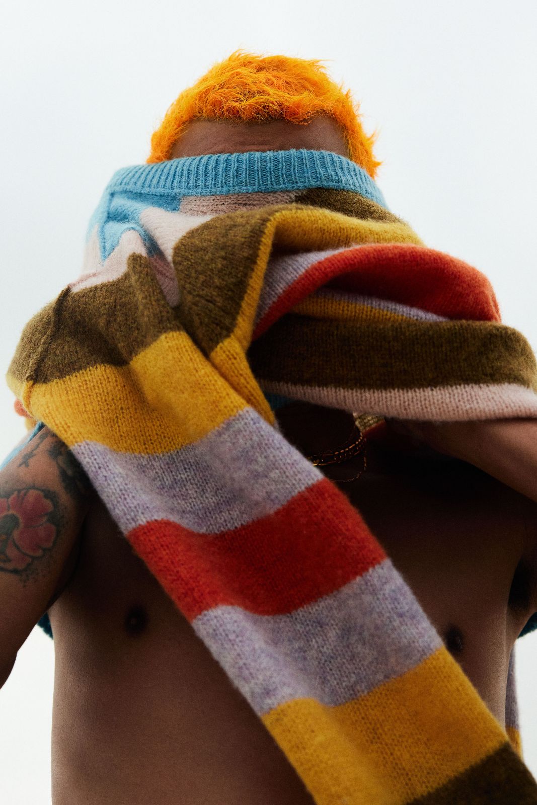 Flako pulls a multi-colored Acne Studios striped sweater completely over his face.