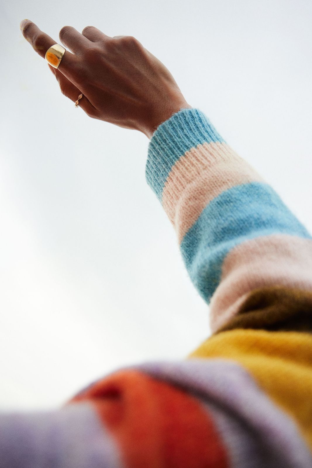 A textured pastel knit sleeve reaching upward against a muted gray background.