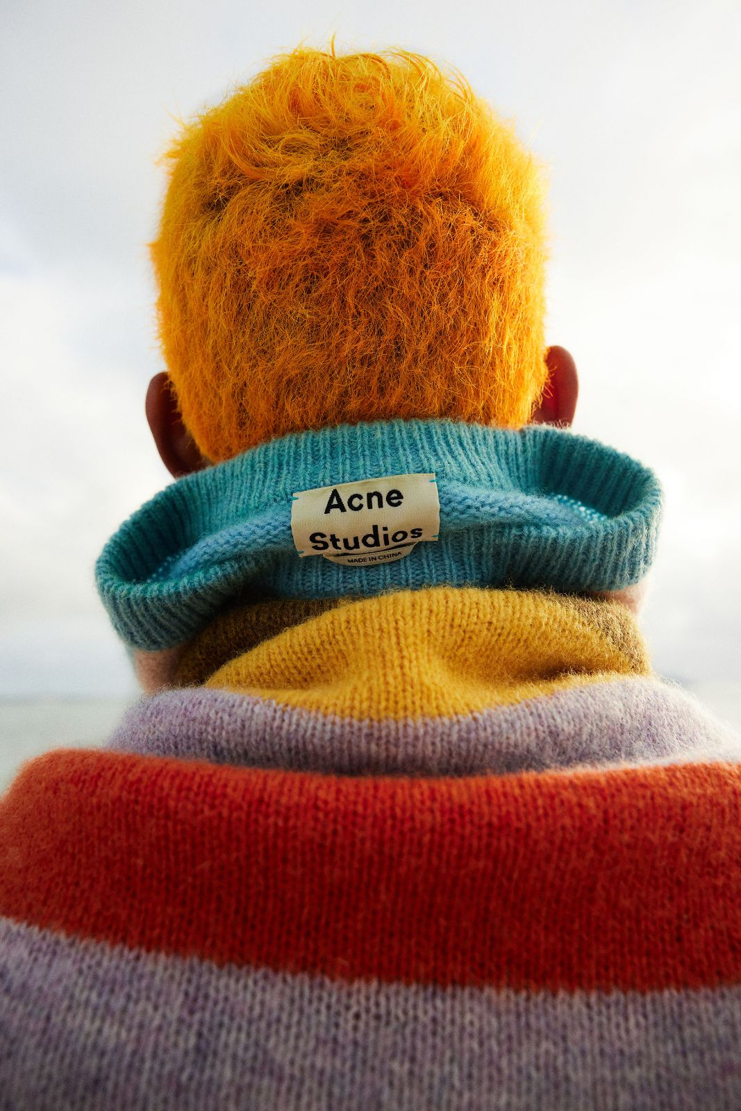 A clear view of the Acne Studios neck tag on a brightly striped knit sweater.