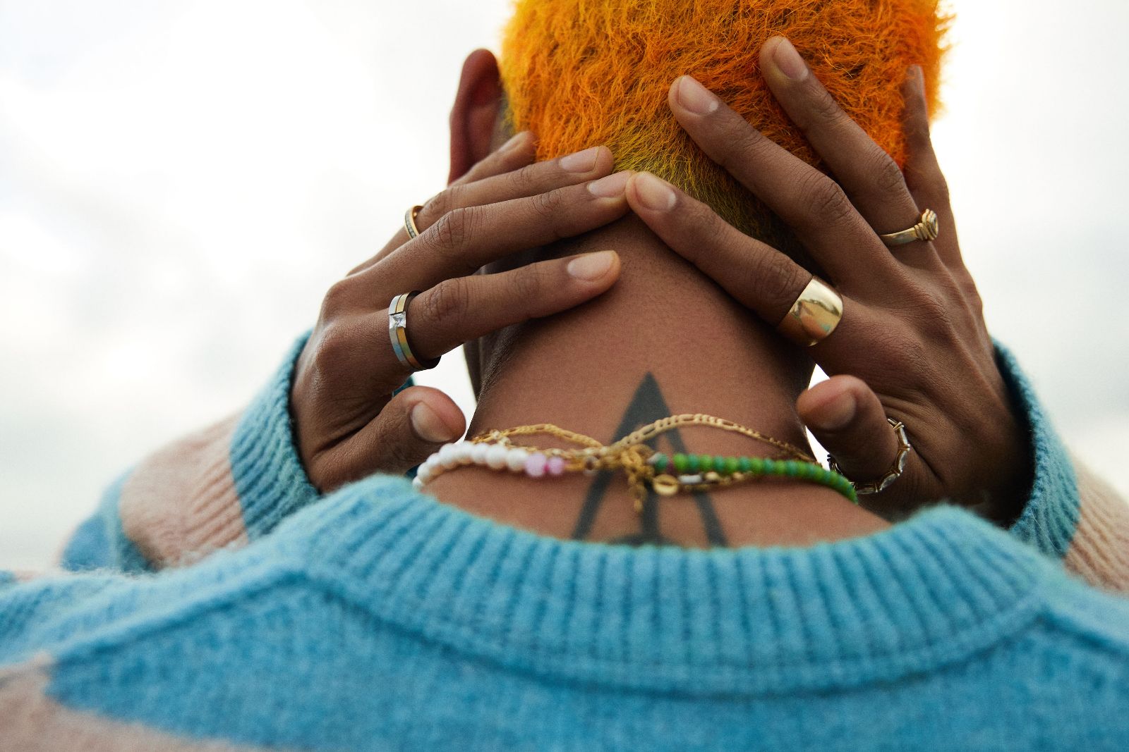Hands gently clasped behind the neck showcasing a sharp dark triangle tattoo.