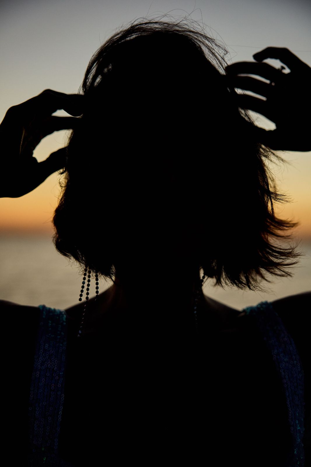 A dynamic silhouette of a woman brushing her hair back against a vivid dawn sky.