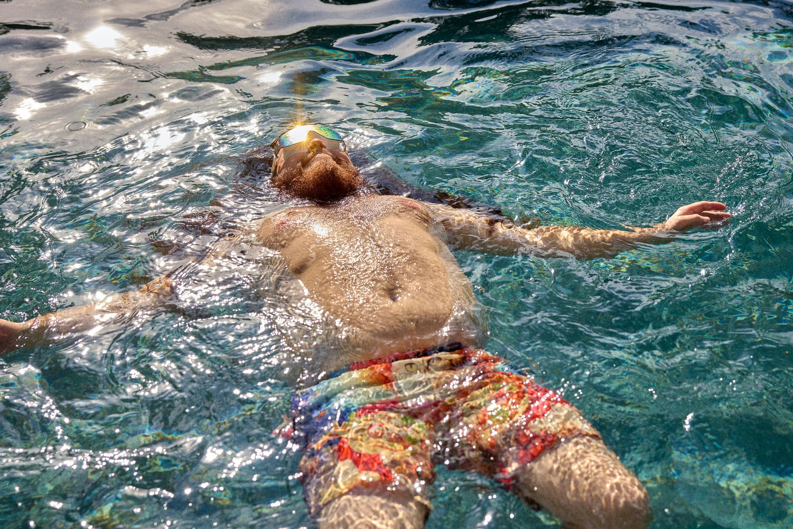 Sunlight catches Alfred's mirrored shades as cool pool water splashes across his face.