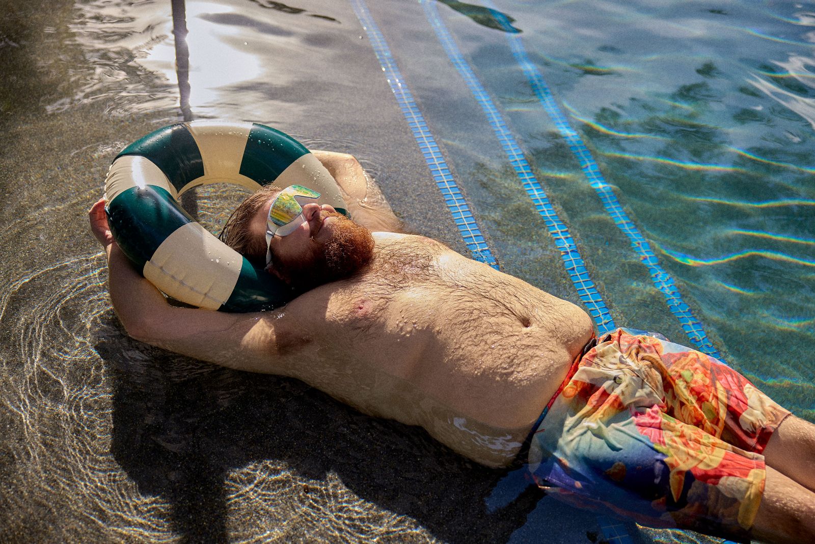 Relaxing completely on a striped inflatable tube with hands casually behind his head.