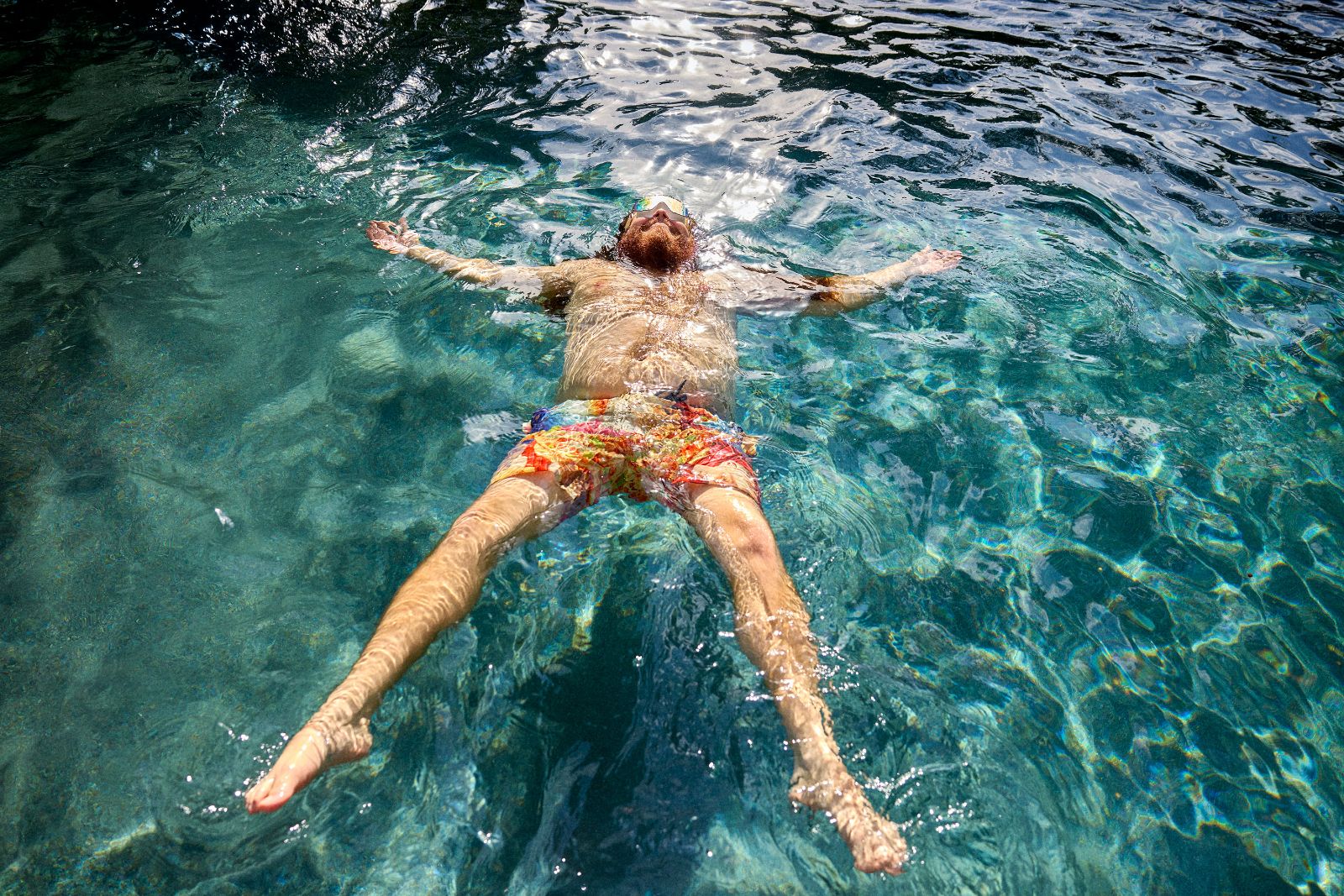Comedian Alfred Diaz floating peacefully in a crystalline Miami pool wearing mirrored sunglasses.