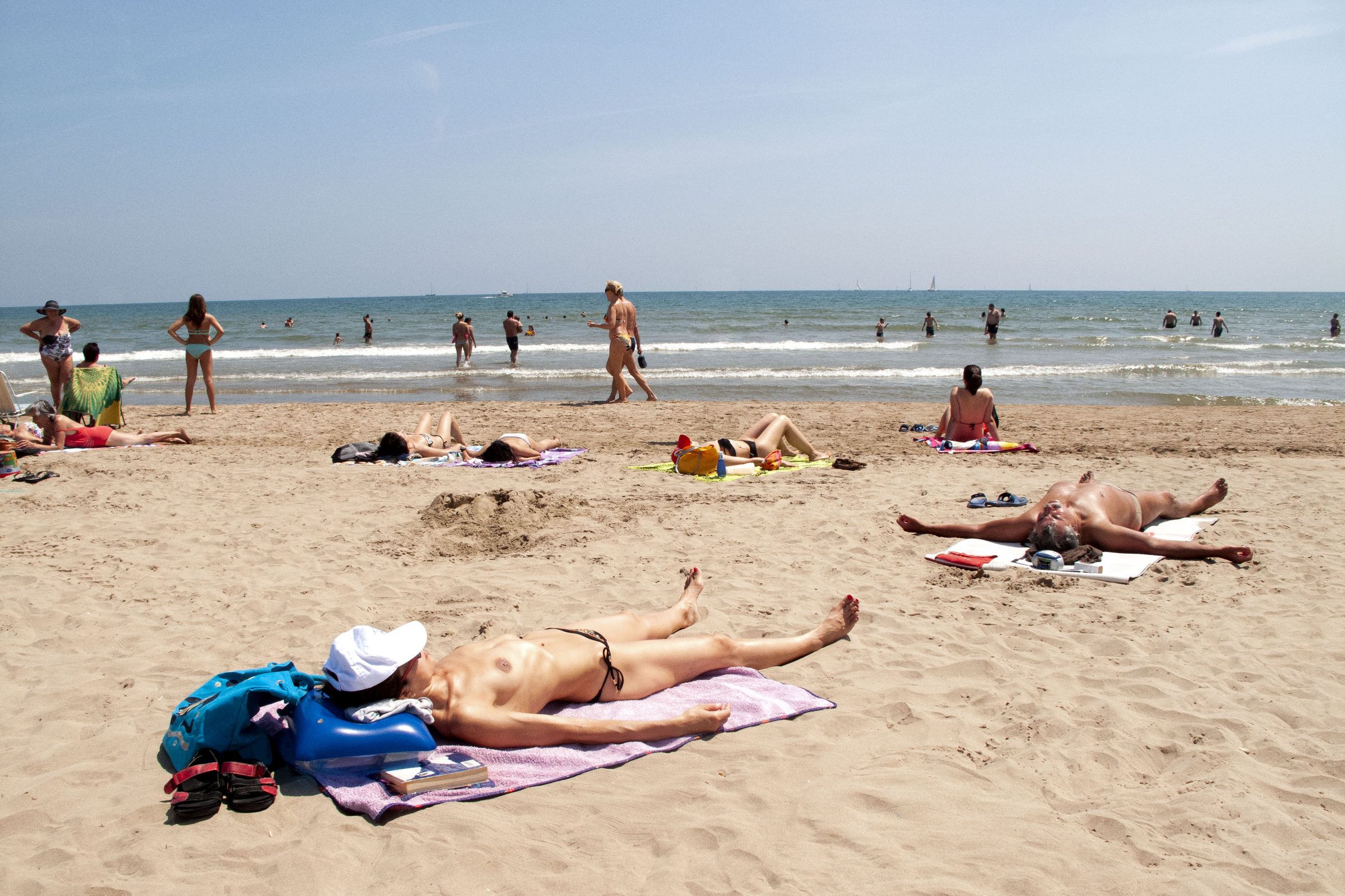 Bathers wade into the Mediterranean while a sunbather naps in a hollow dug into the sand.
