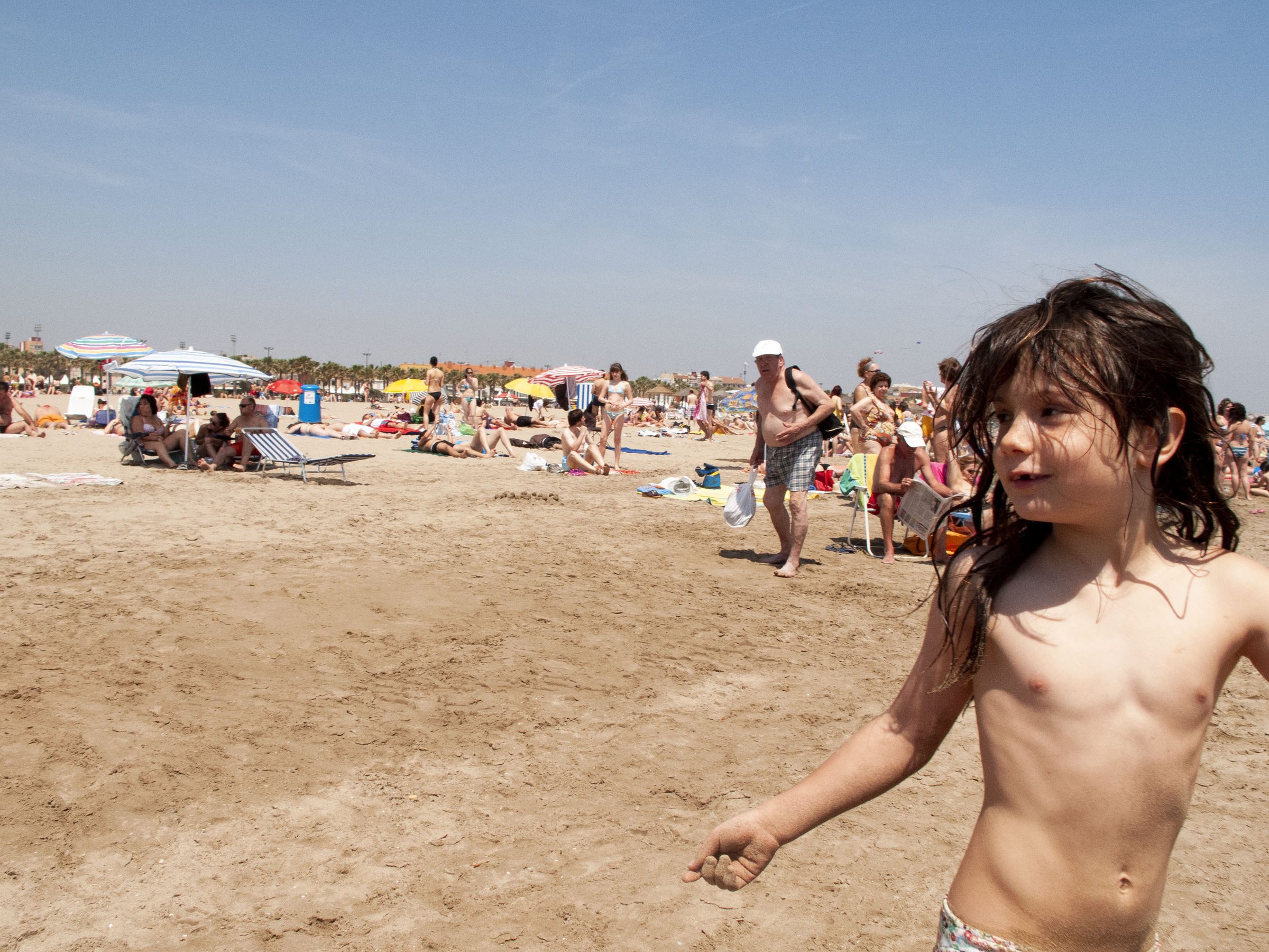 A drenched kid marches up the sand, hair slicked by the last wave.