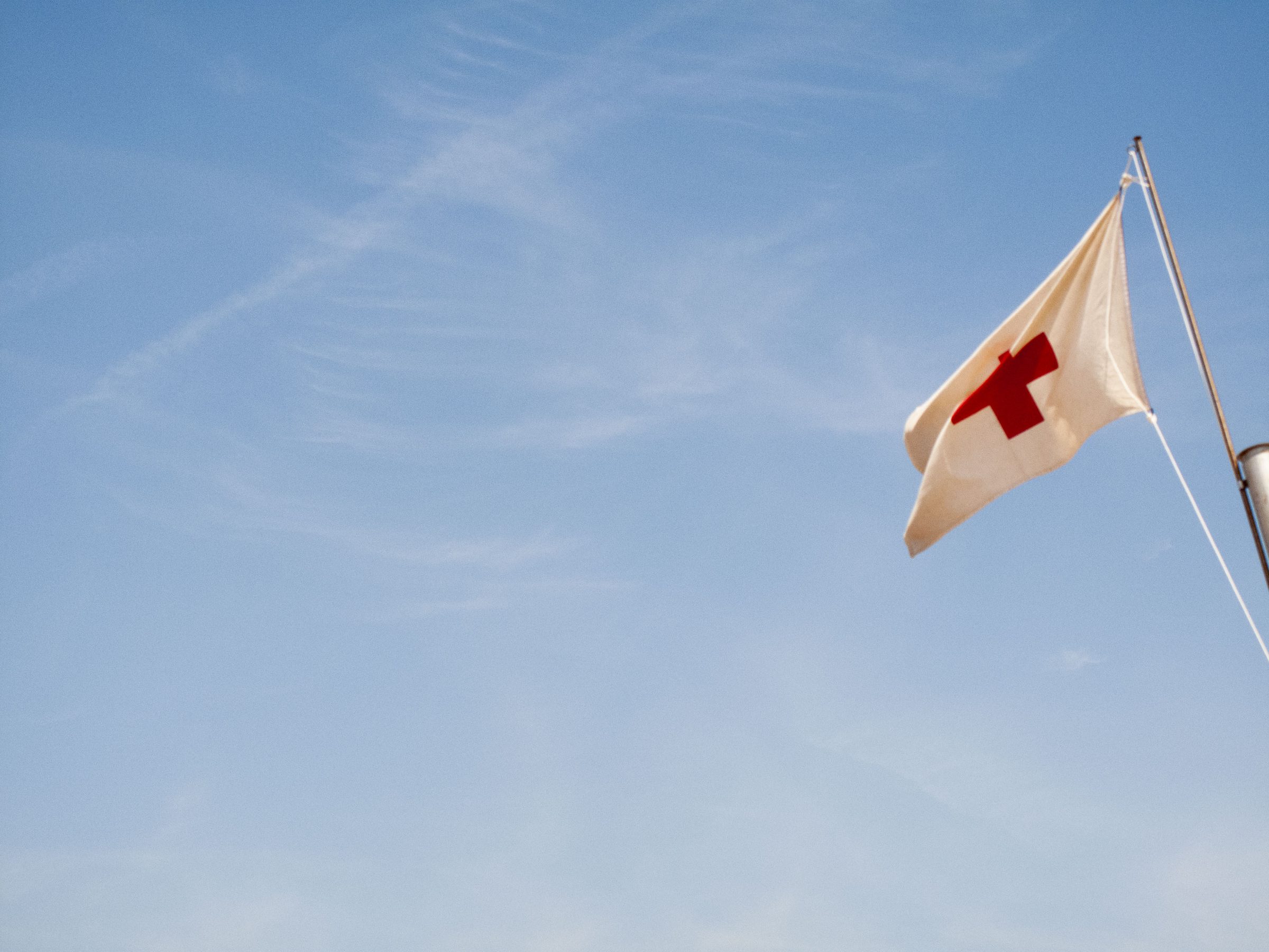 A Red Cross flag snaps against the empty summer sky.