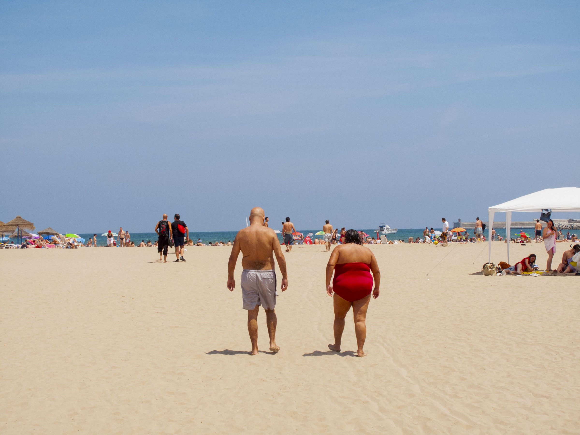 Two bathers cross the open sand toward the water, matched in stride.