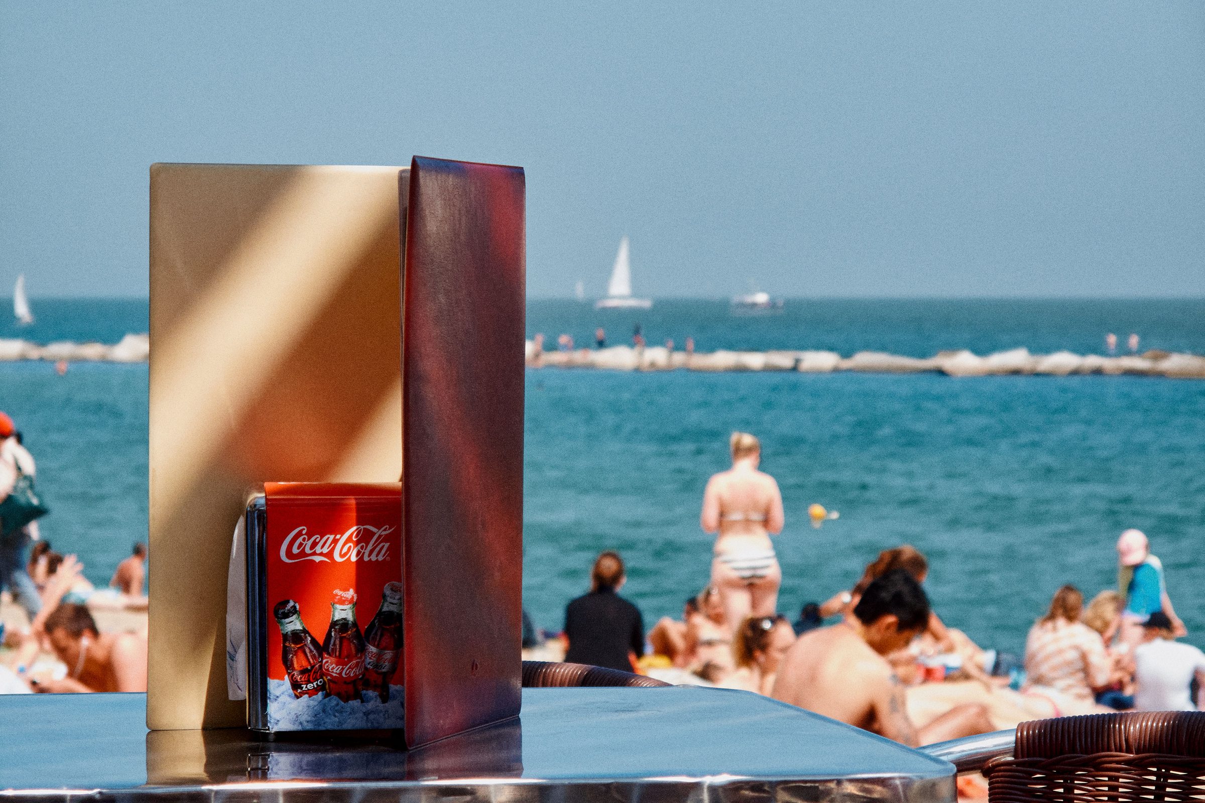 A chilled Coca-Cola sweating on a beach bar table above the crowded Barceloneta shoreline.