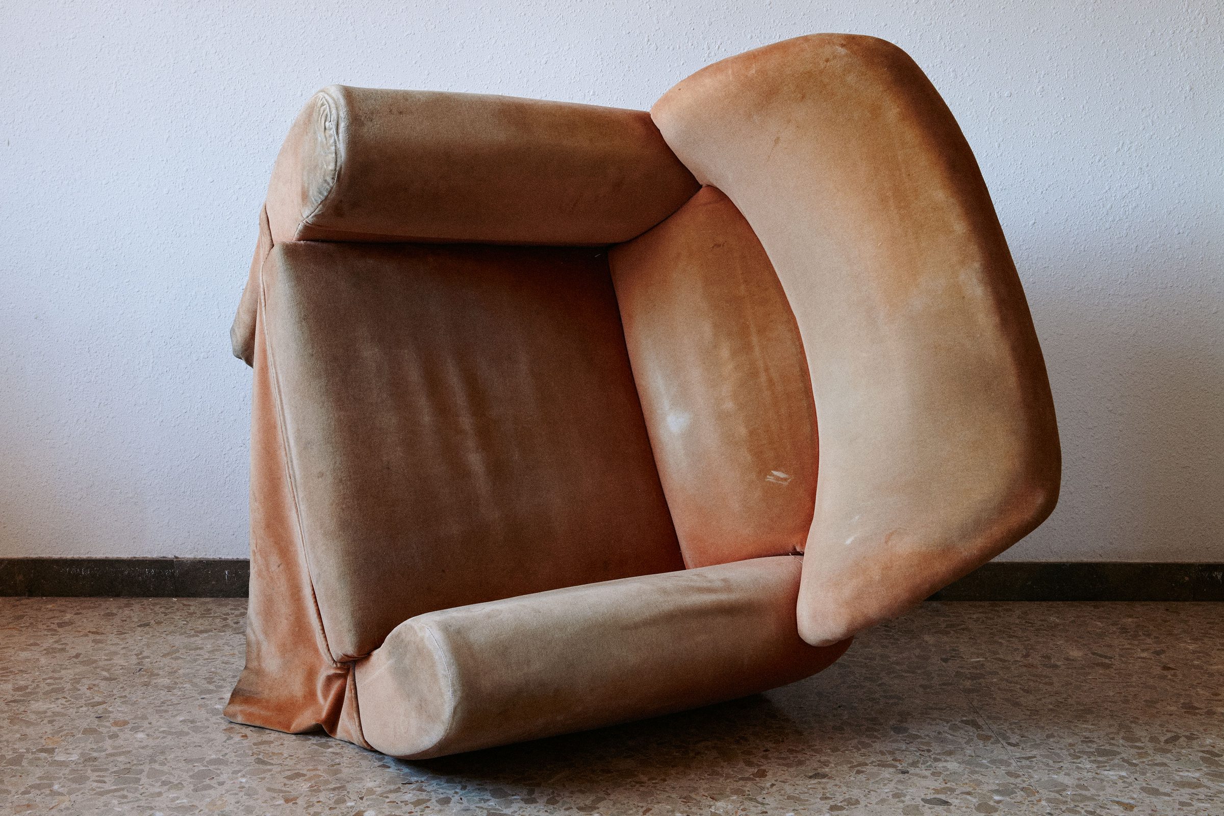 A worn leather armchair tipped on its side against a bare interior wall in Barcelona.