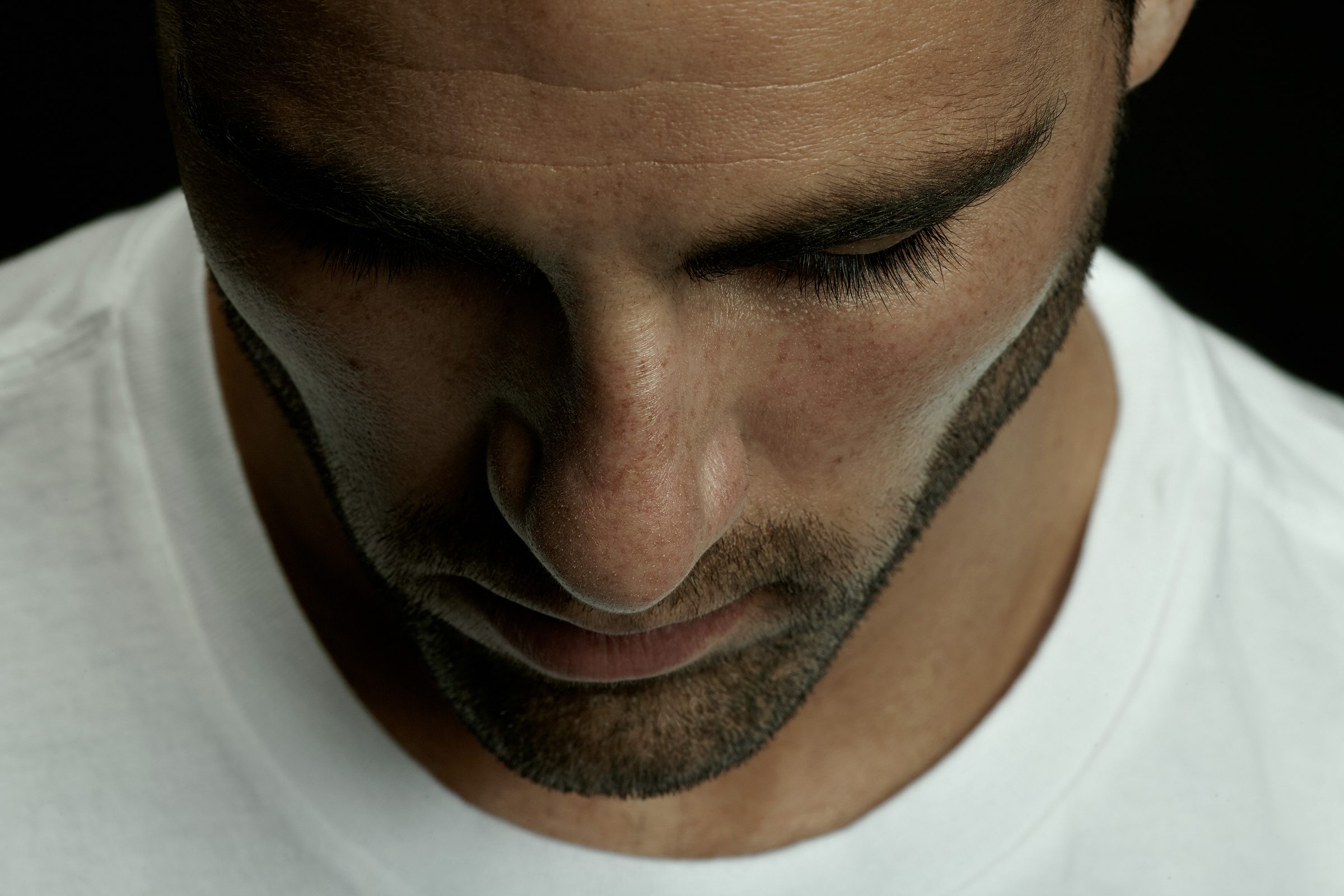 Michael's downturned face in a white tee, lashes and beard-line in sharp macro relief.